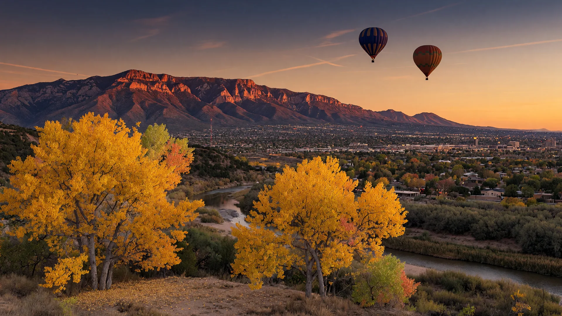 Golden cottonwoods along the Rio Grande with the Sandia Mountains glowing at sunset and hot air balloons in the distance