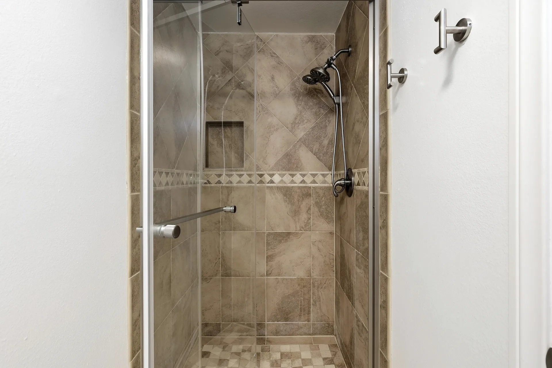 Tiled shower at 8 Silverwood with large-format beige tiles, a mosaic accent strip, and a glass door