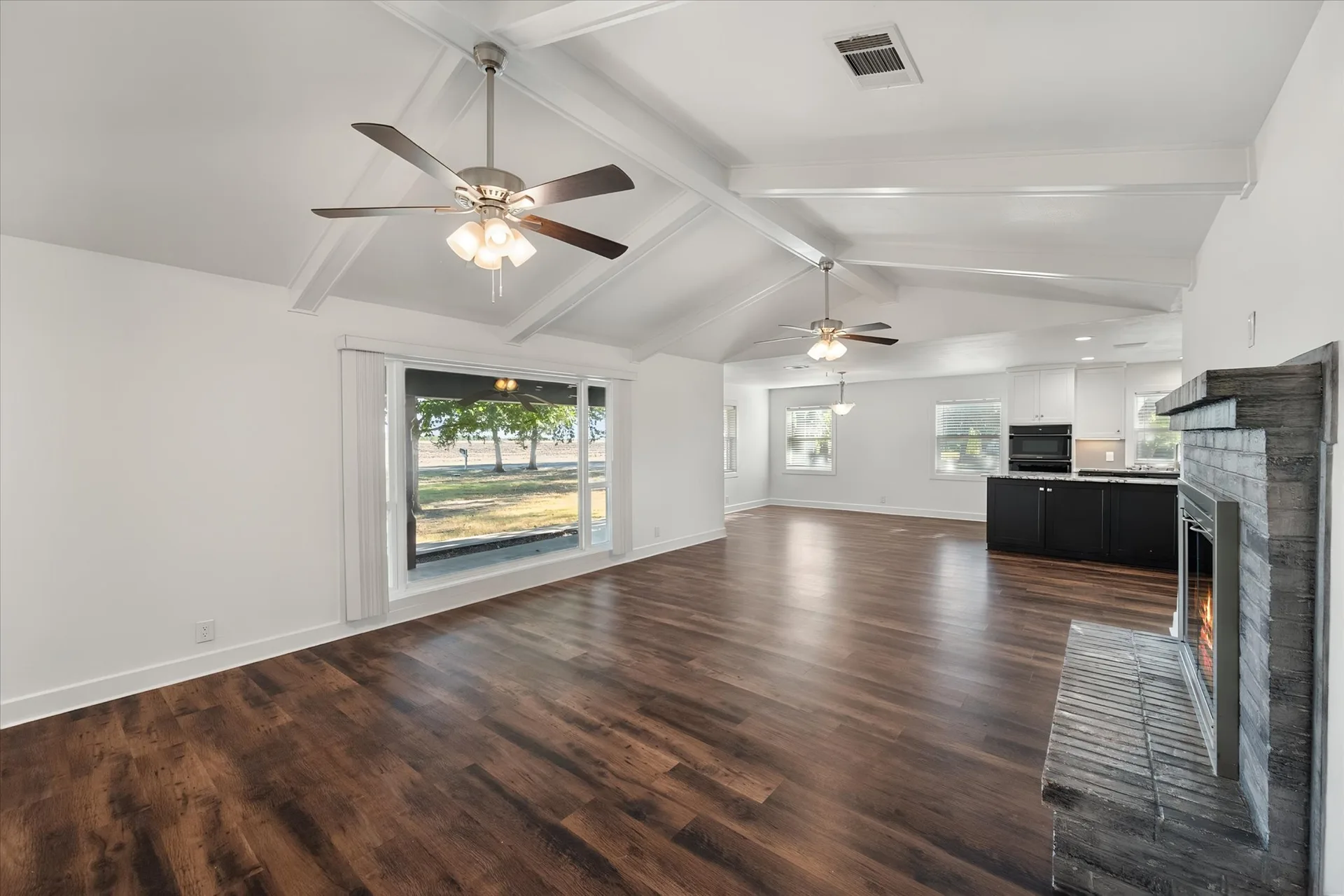 Wide view of the open living area with a brick fireplace and beamed ceiling