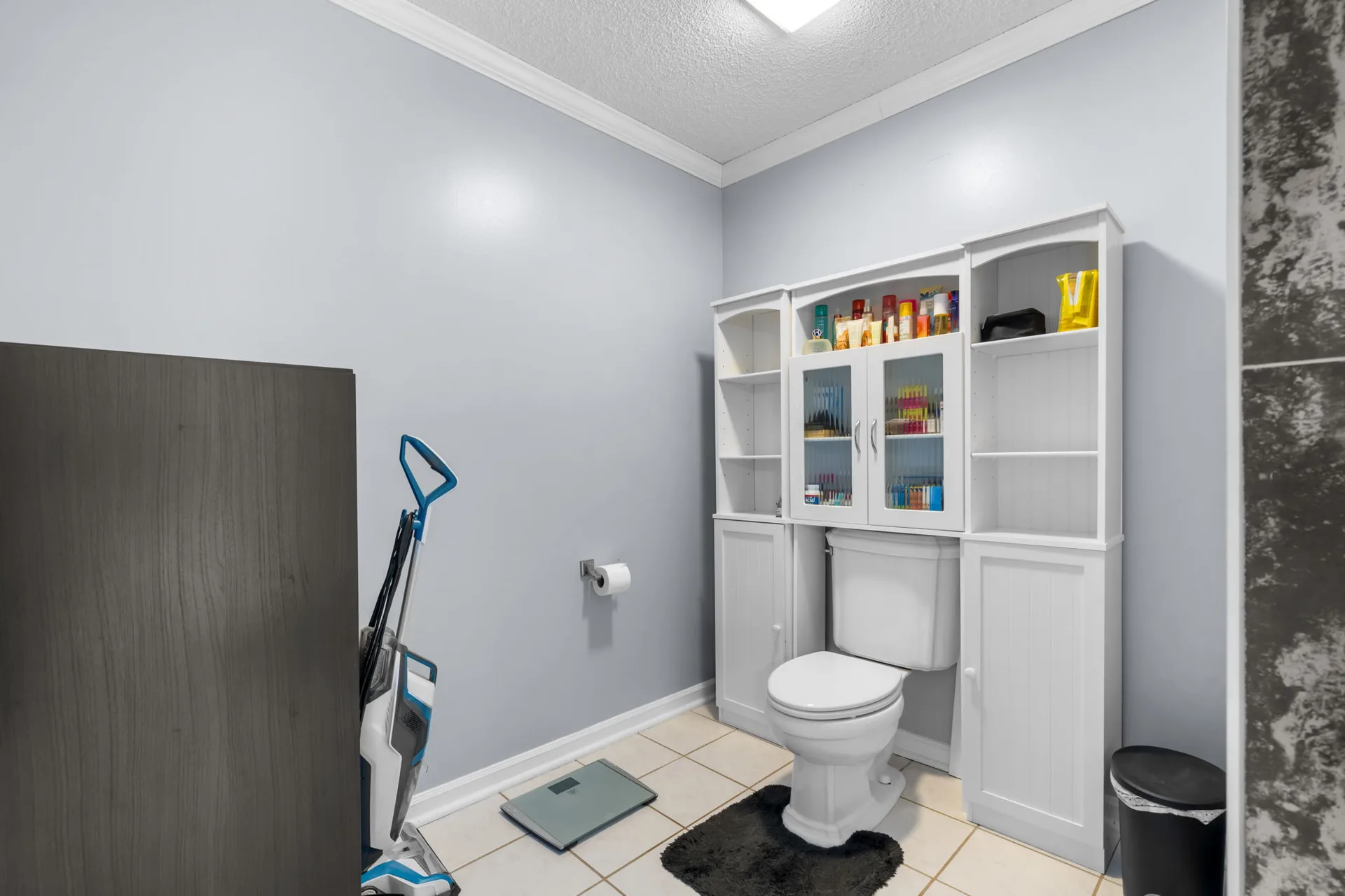 Primary bath with a white built-in storage unit over the toilet and tiled floor