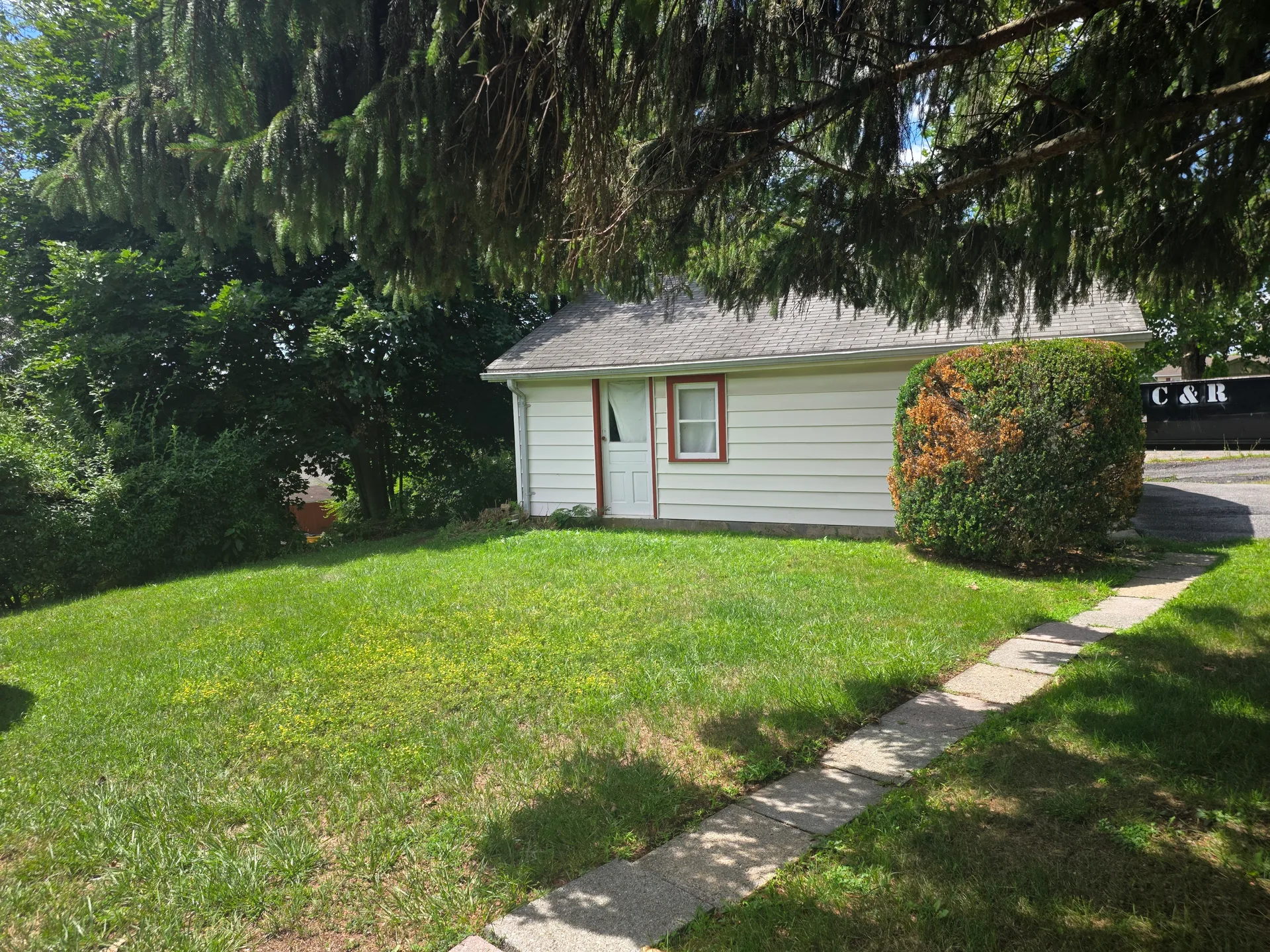 Side view of detached garage with vinyl siding under shade of a large tree