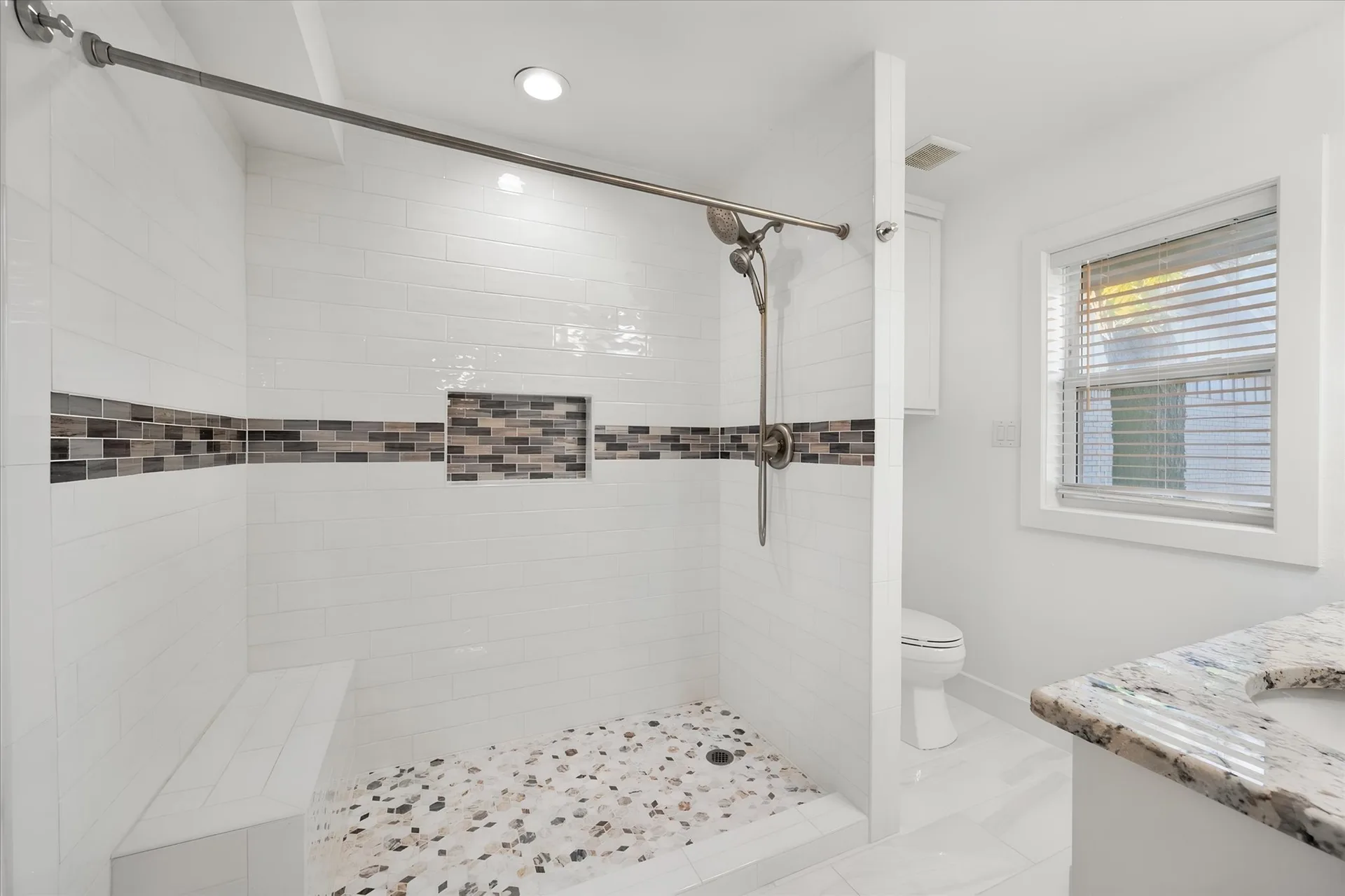 Renovated walk-in shower with pebble flooring and a mosaic tile accent strip