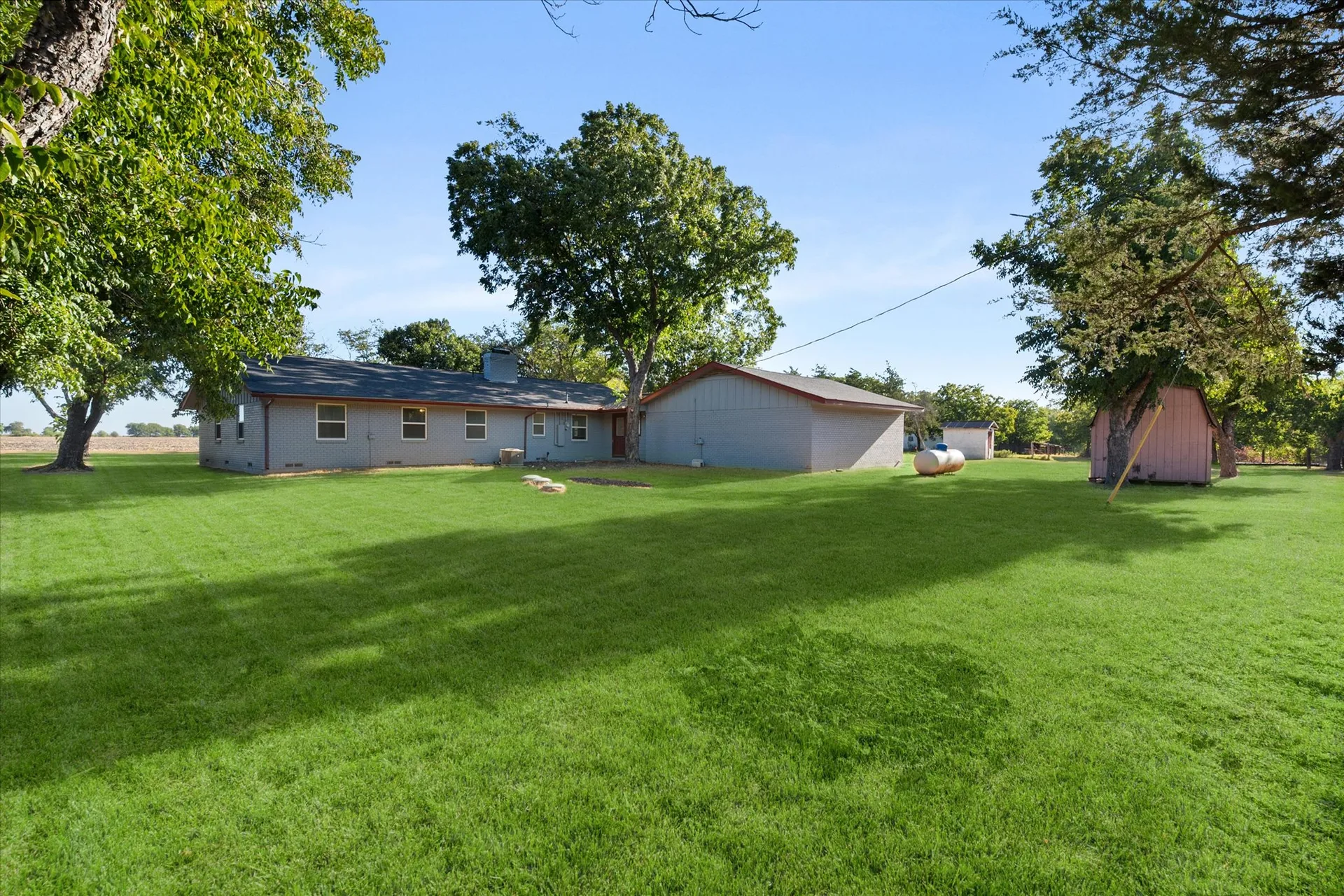 Backyard of the ranch home with open lawn, mature trees and a small shed