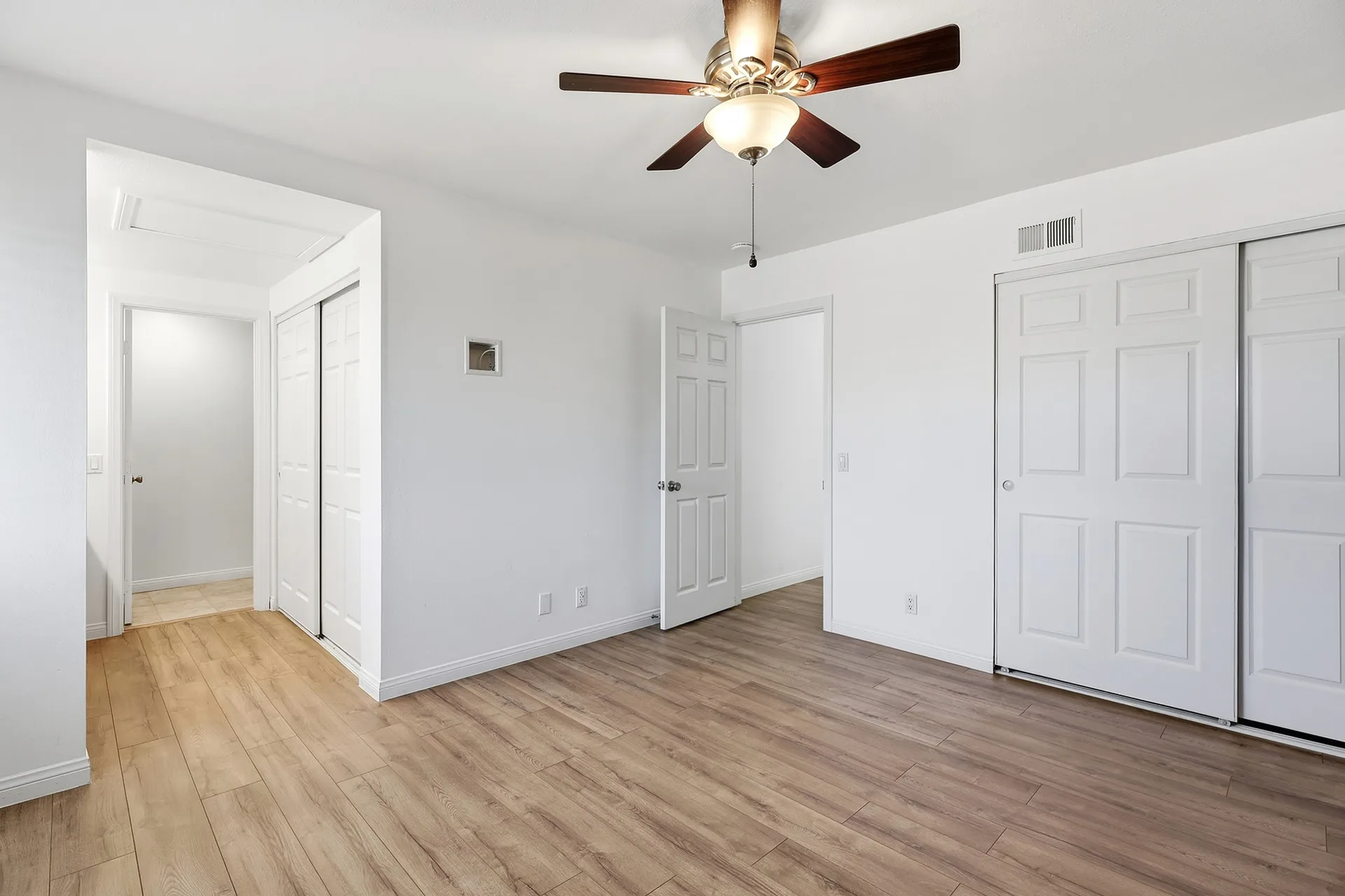Primary bedroom at 8 Silverwood with light wood plank flooring, white walls, and a ceiling fan