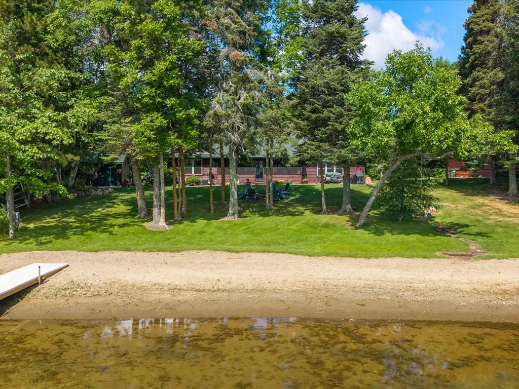 The property seen from the water with sandy beach, dock, and firepit grounds