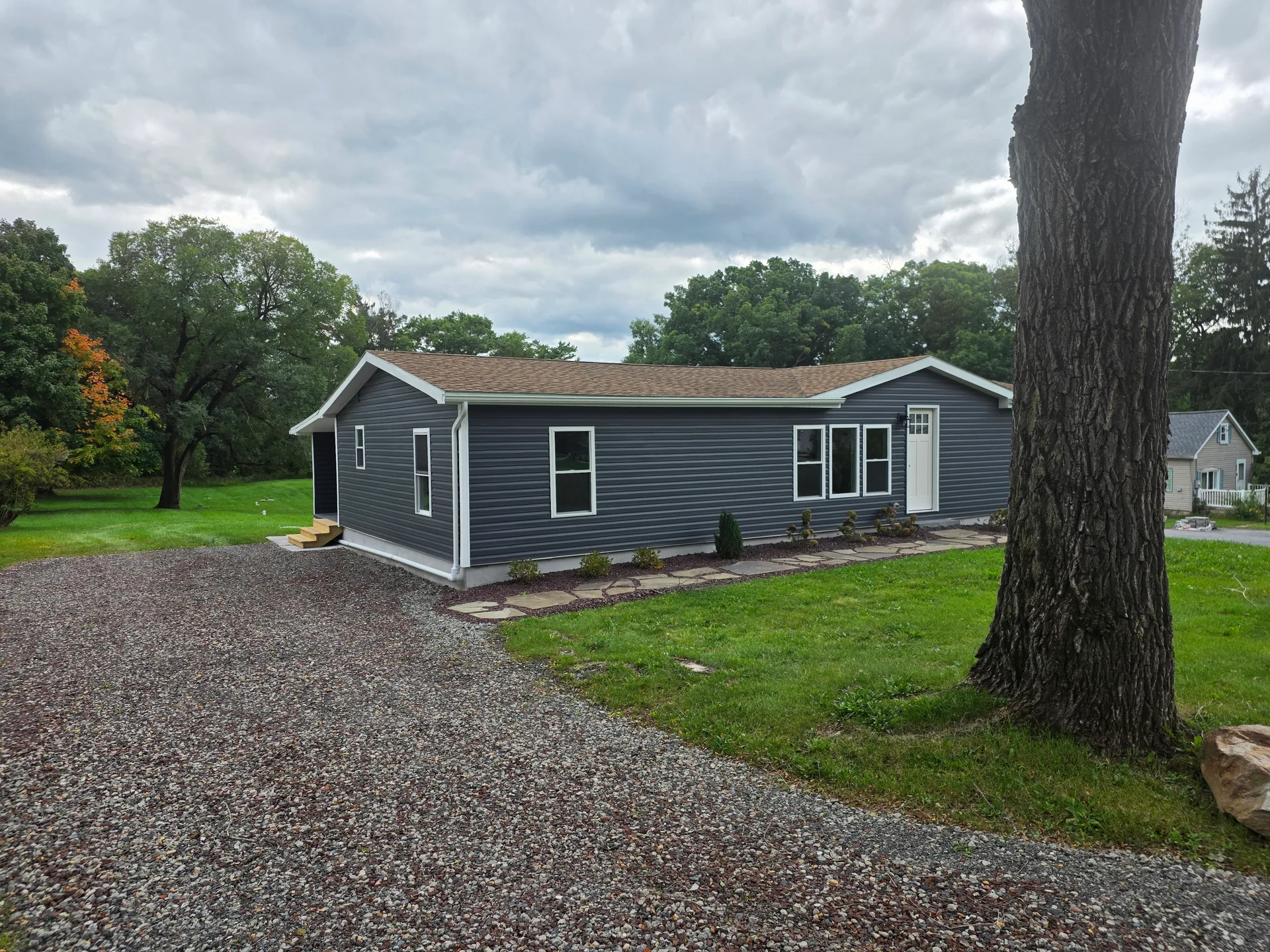 Side facade of the ranch home with mature landscaping and gravel driveway