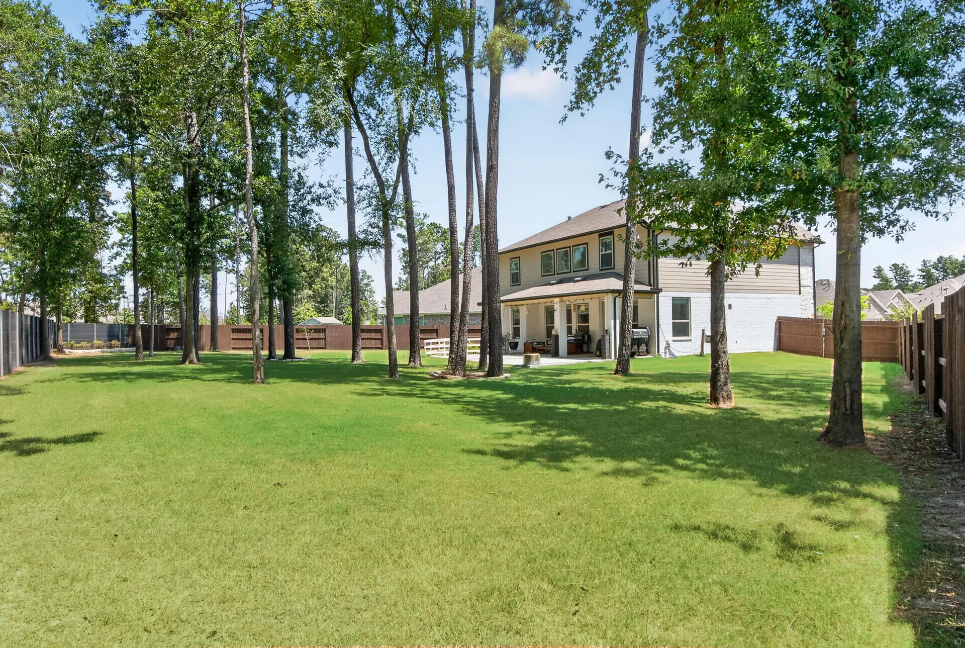 Rear view of the home with a large lawn and concrete covered patio under mature trees