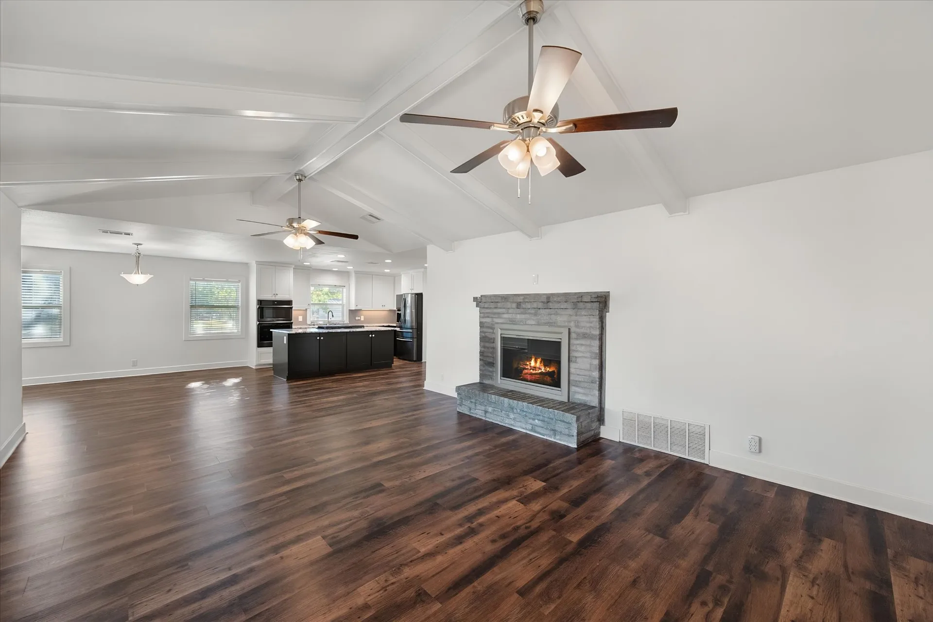 Open living area flowing into the kitchen with vaulted beams and a stone-veneer fireplace