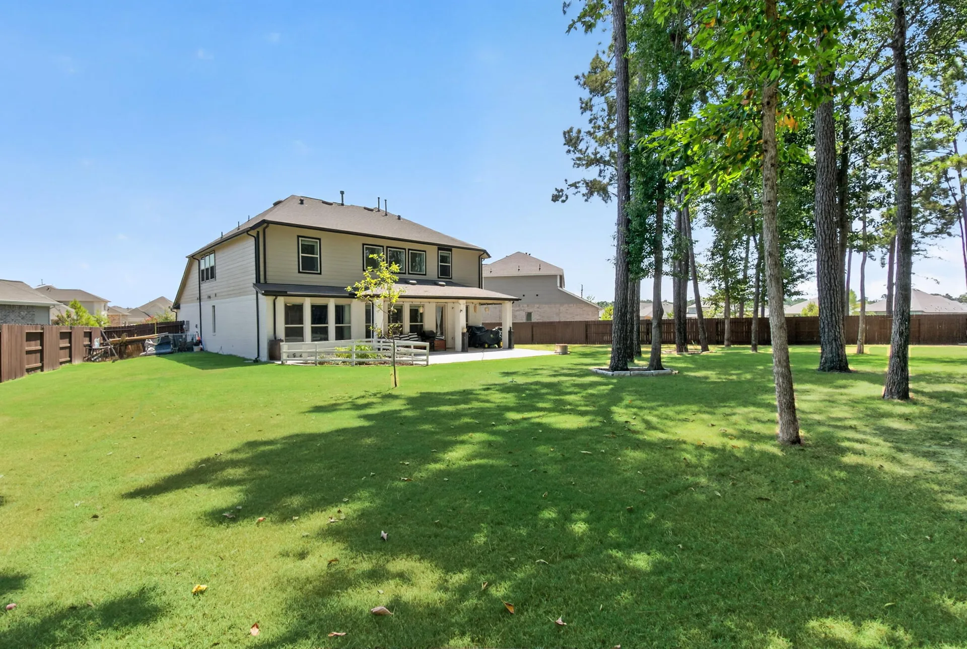 Expansive backyard with covered patio, broad lawn, and mature pines behind the two-story home