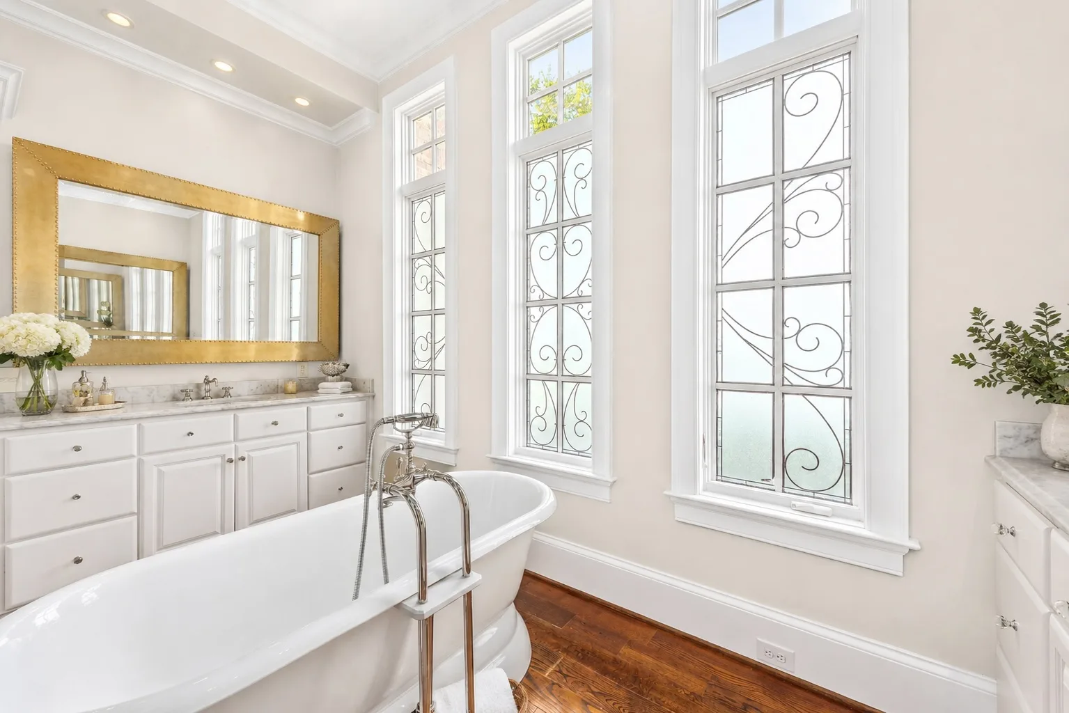 Primary bathroom with soaking tub, marble countertops, and gold-framed mirror