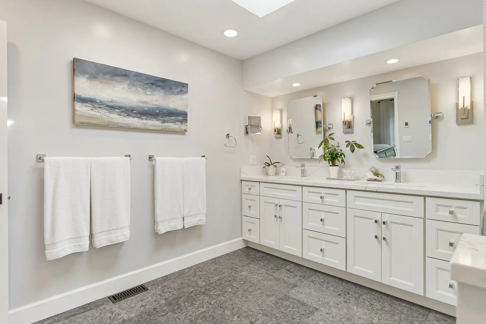 Primary bathroom vanity with white cabinetry, marble countertops and dark tile flooring