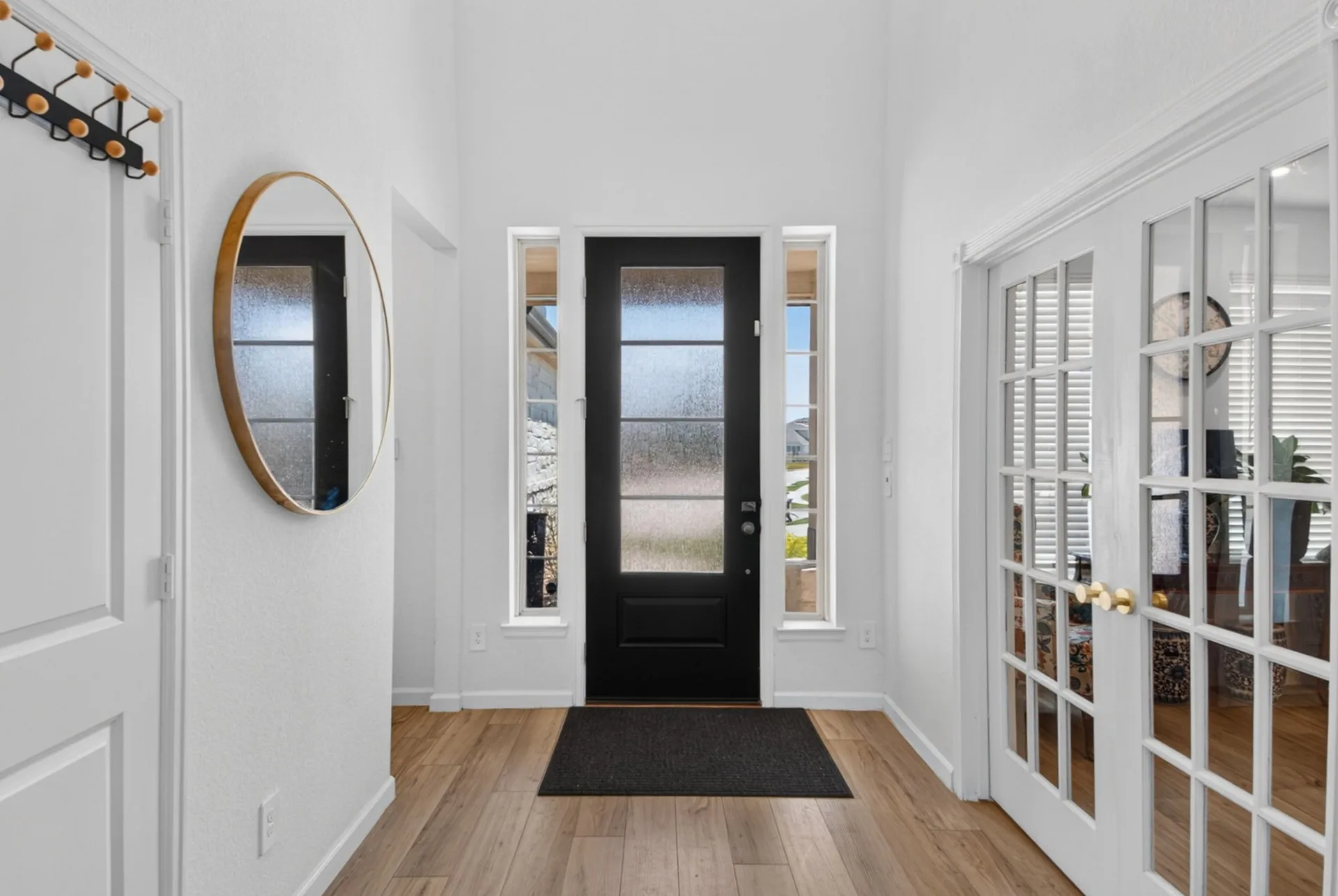 Bright front foyer with the black front door, side lights, and light wood flooring
