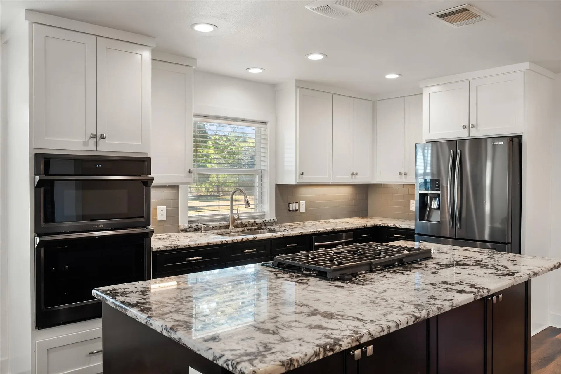 Kitchen island with granite counters, double wall ovens and a tile backsplash