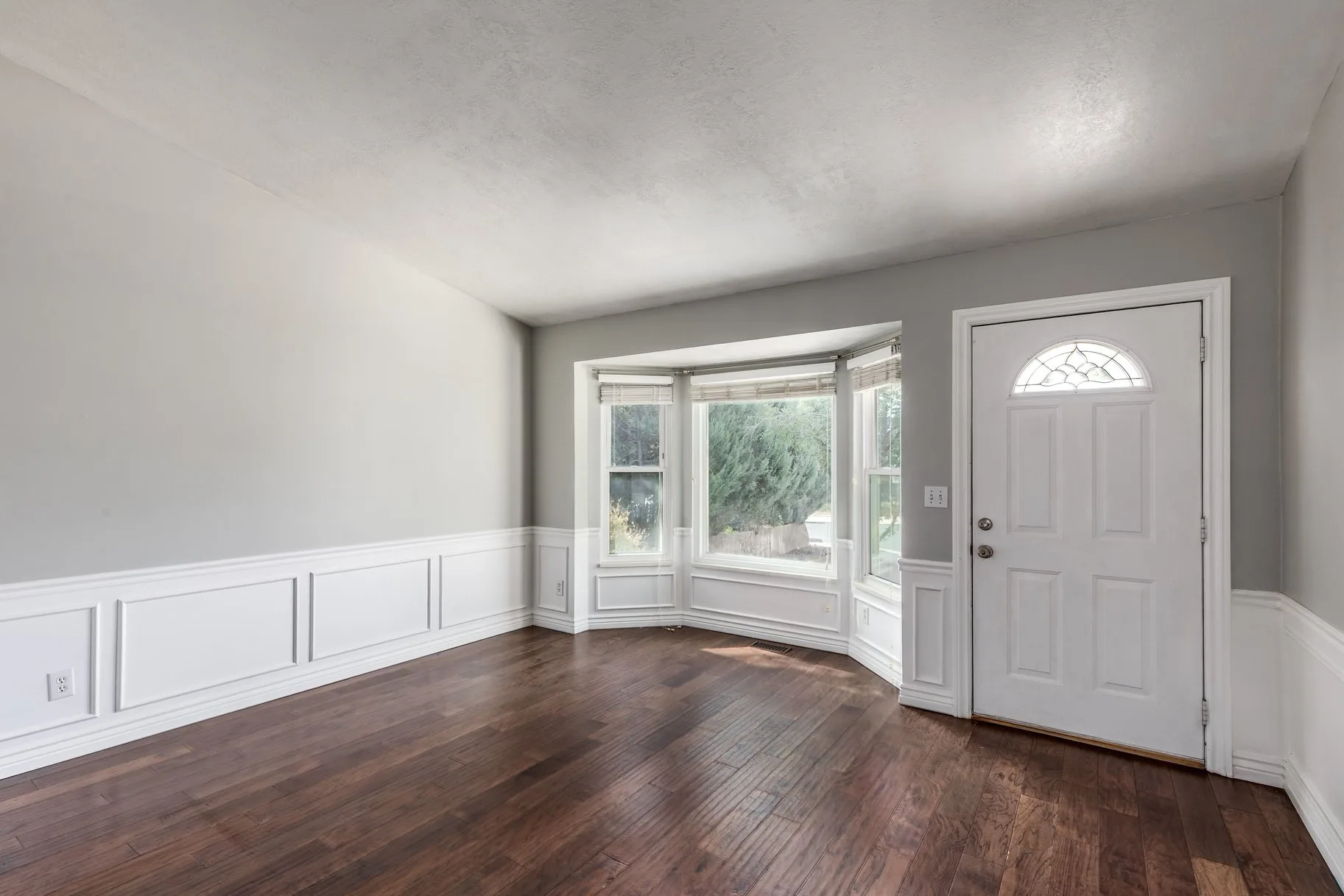 Living room with bay window, wainscoting, and hardwood floors