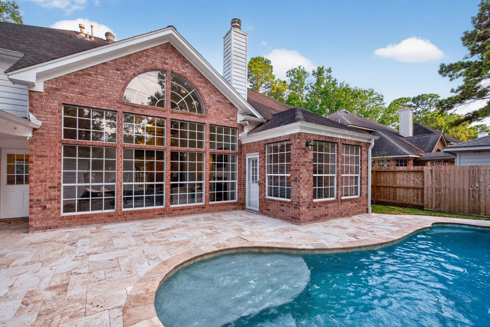 Backyard of 4211 Brook Shadow Dr with the pool, stone patio, and two-story window wall