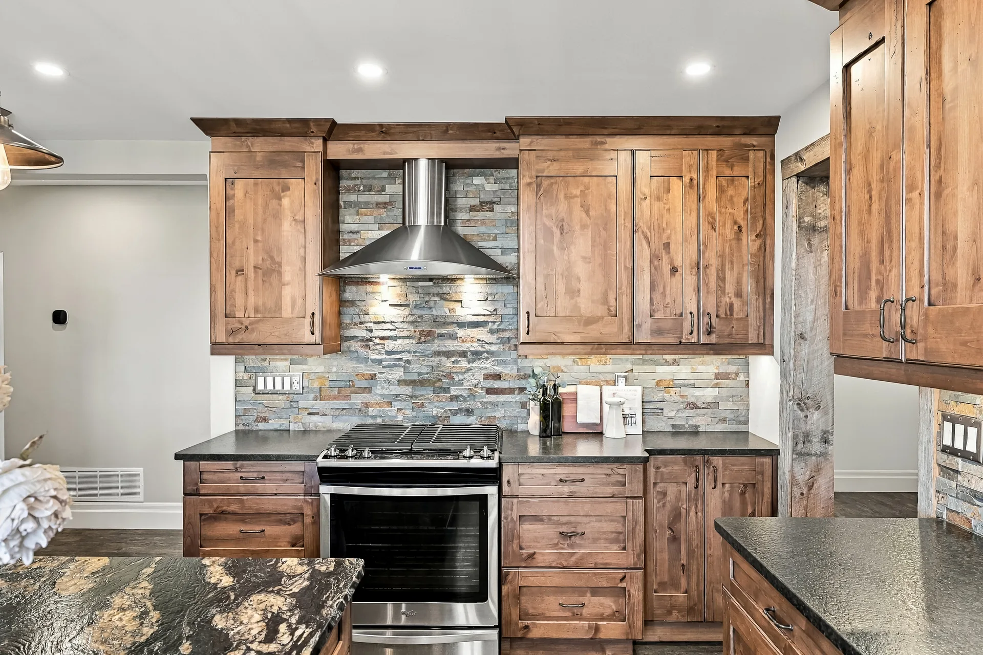 Stove wall with stacked stone backsplash and wood cabinetry