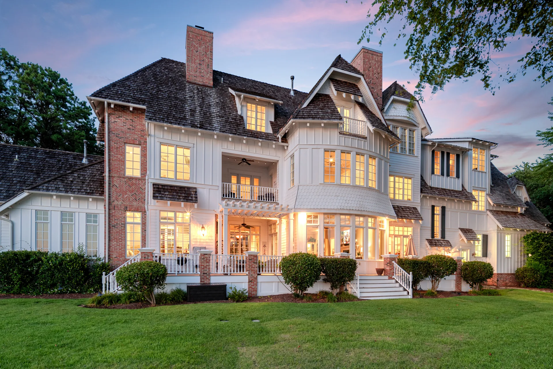 Rear exterior facade at dusk with terrace, covered porch, and landscaped lawn