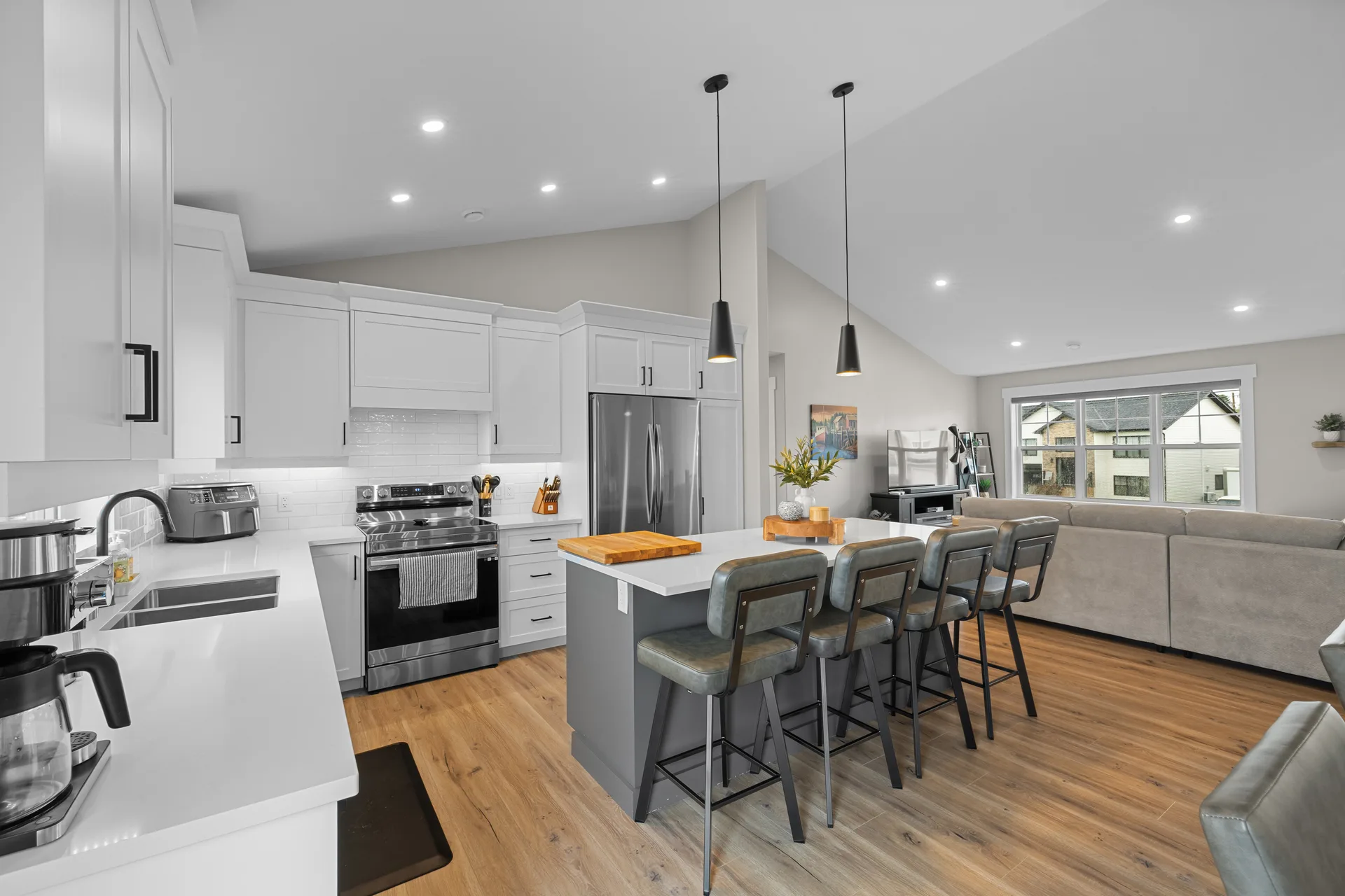 Open-concept kitchen and living area with vaulted ceilings, white cabinetry, slate grey island, and light wood flooring