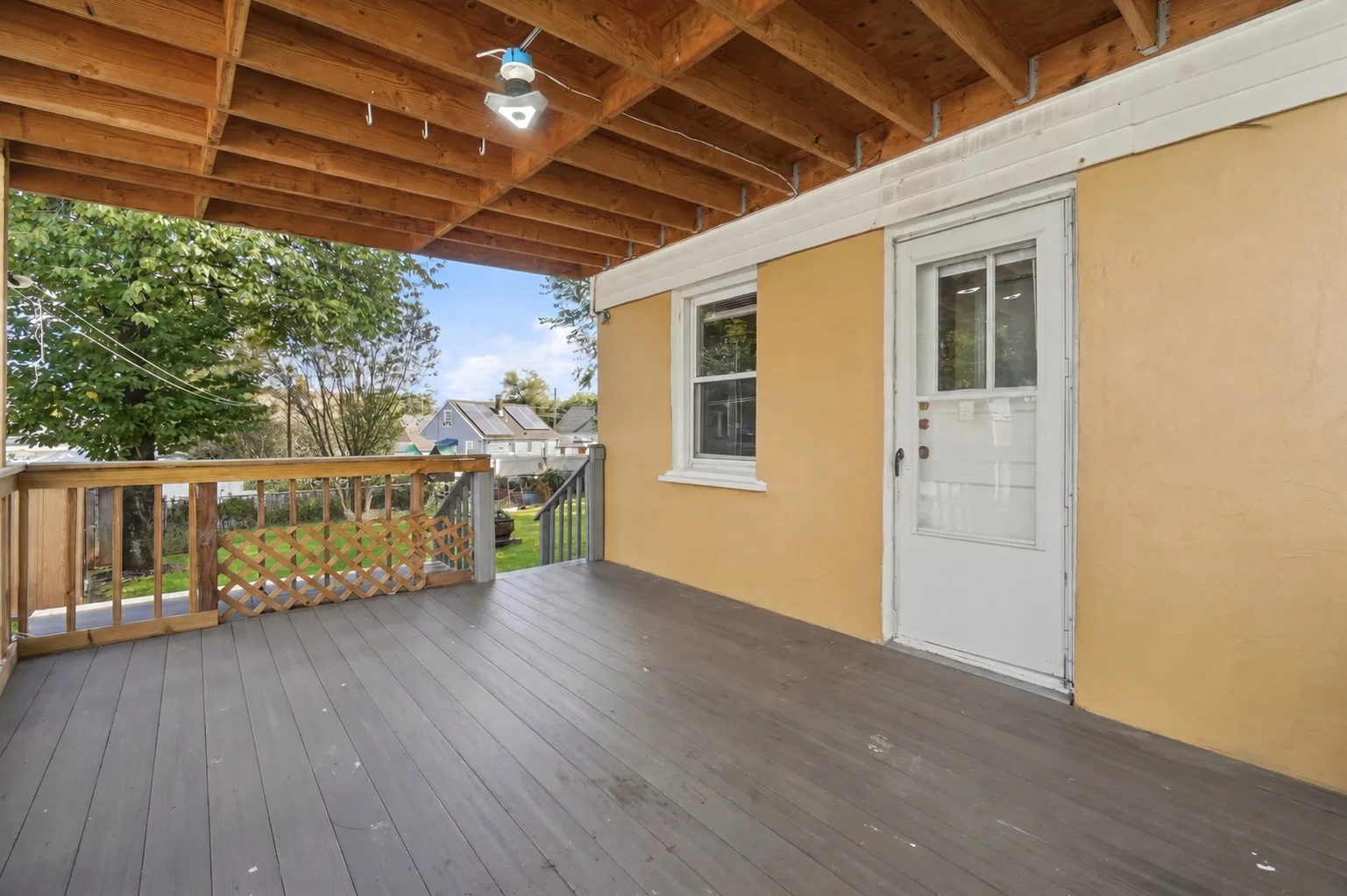 Covered backyard deck with grey composite decking and yellow stucco siding