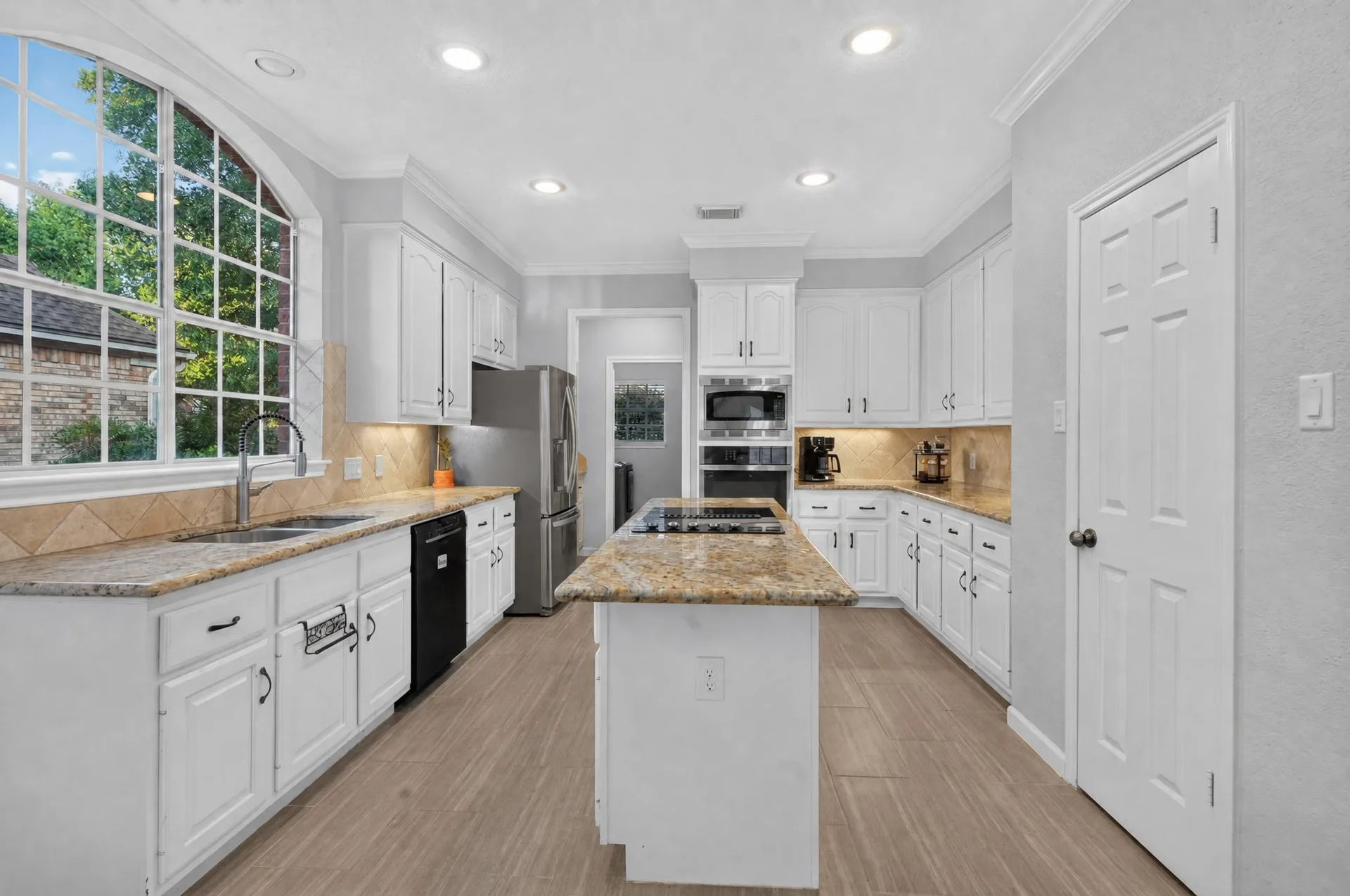 Kitchen with white cabinets, granite counters, a large island, and an arched window