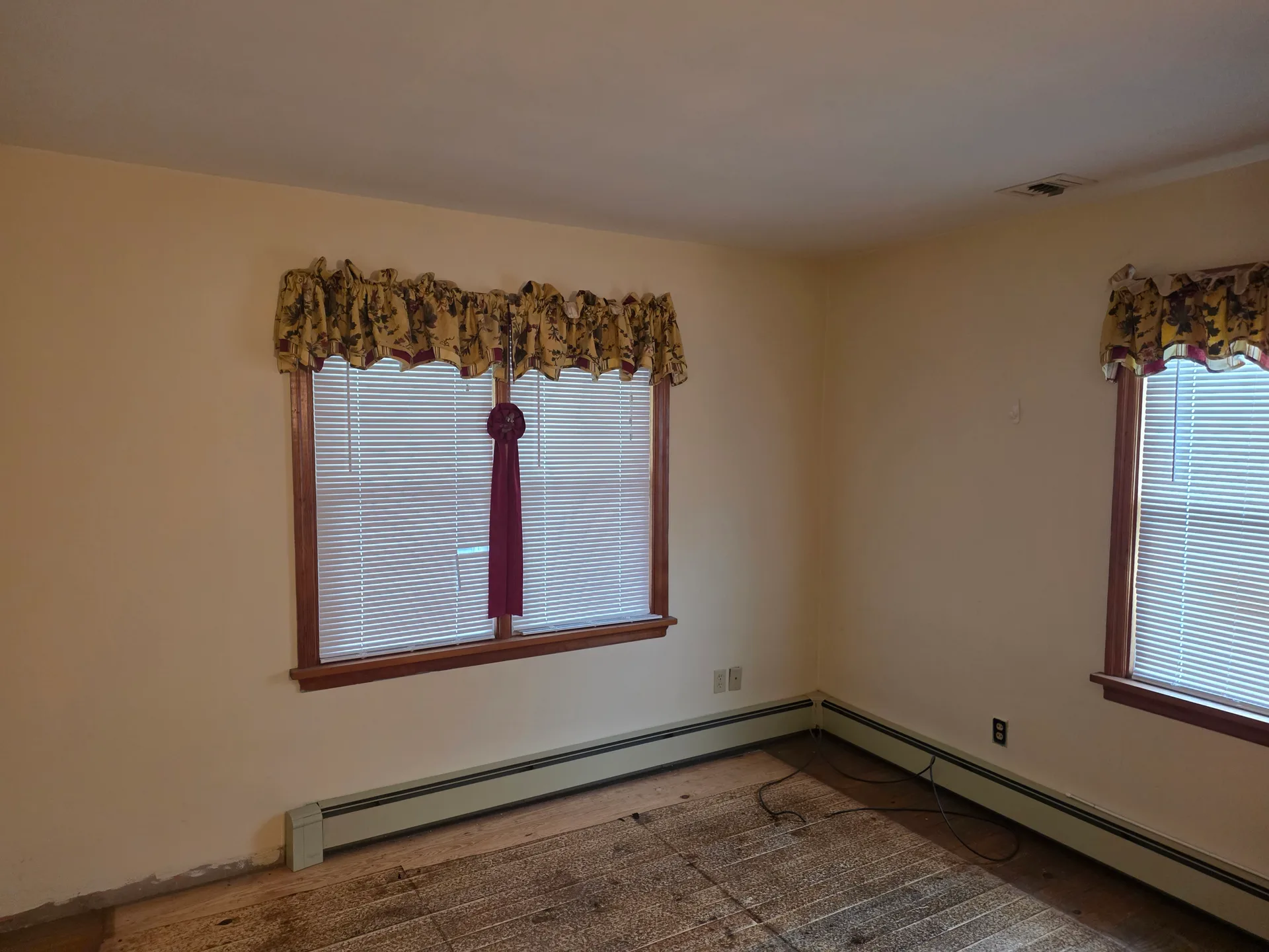 Empty living room with beige walls, hardwood flooring, and baseboard heating