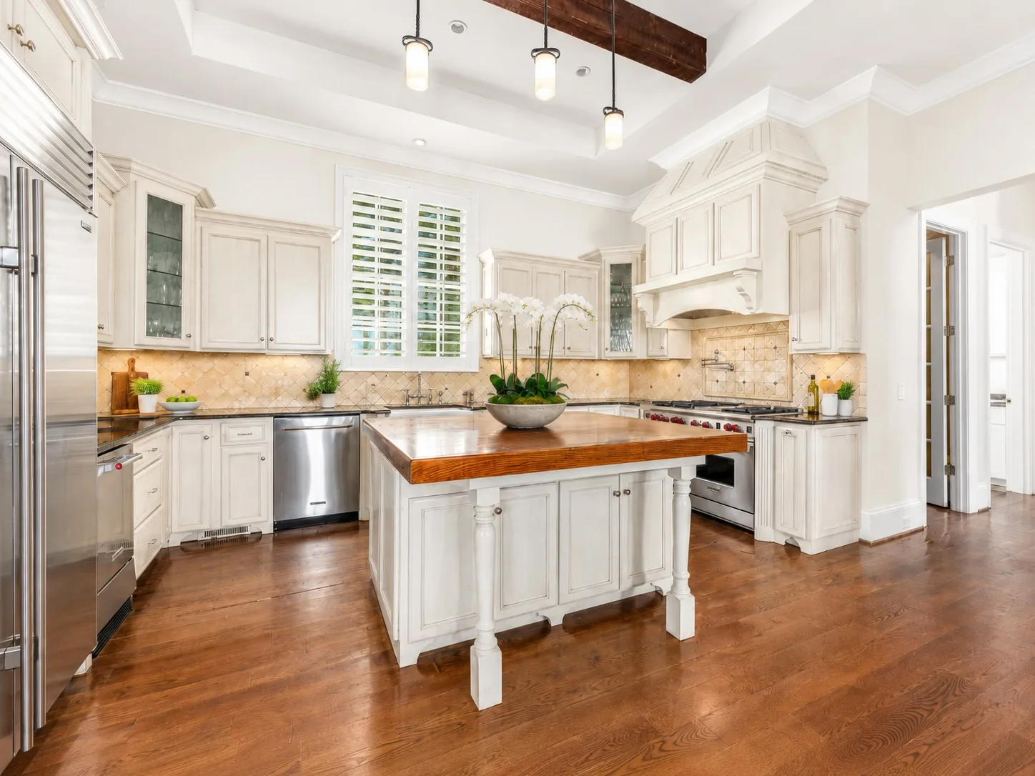Chef's kitchen with white cabinetry, stained wood island, and dark ceiling beam
