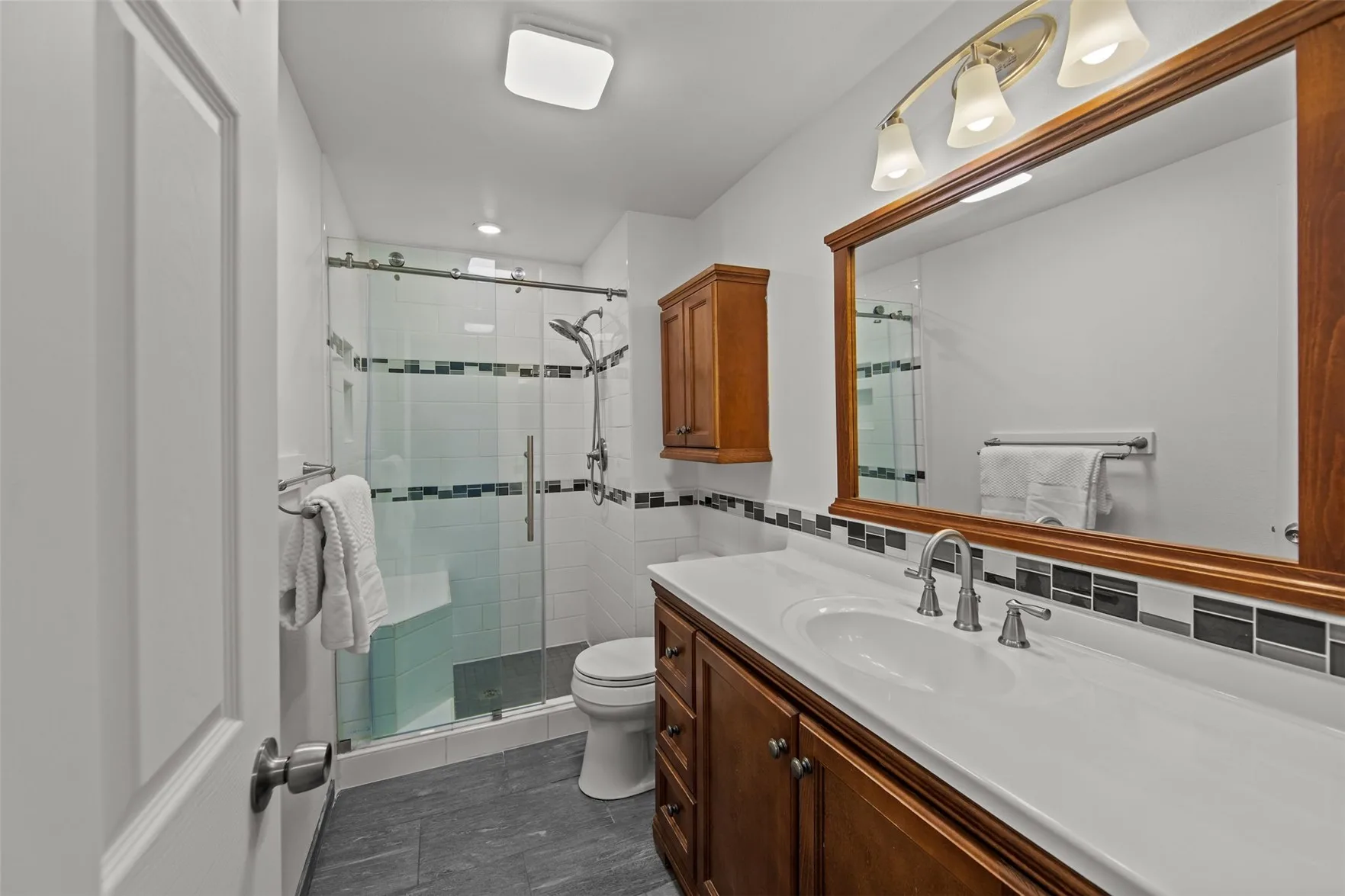 Remodeled bathroom with glass-enclosed shower and wood vanity