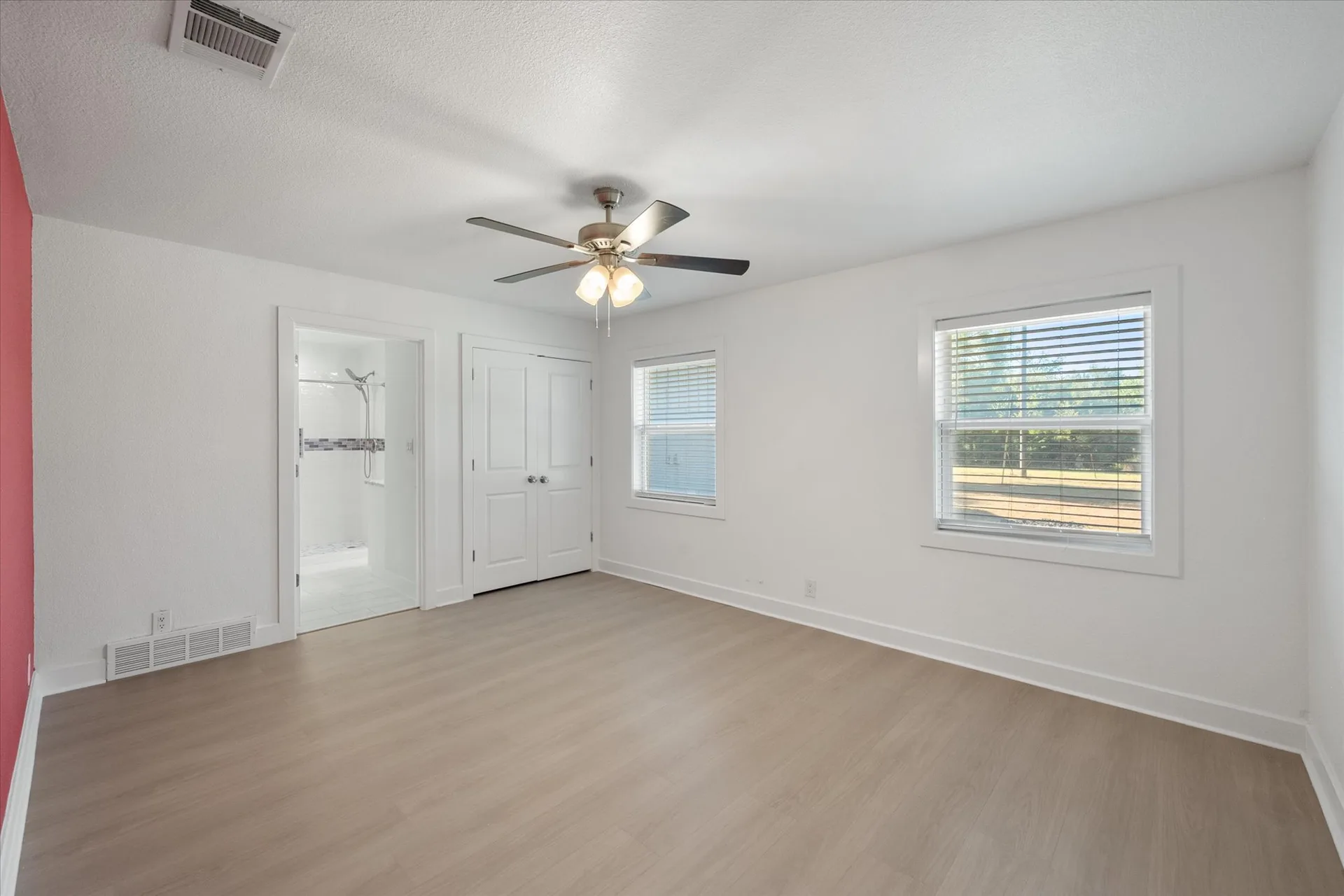 Renovated primary bedroom with a red accent wall and light wood flooring