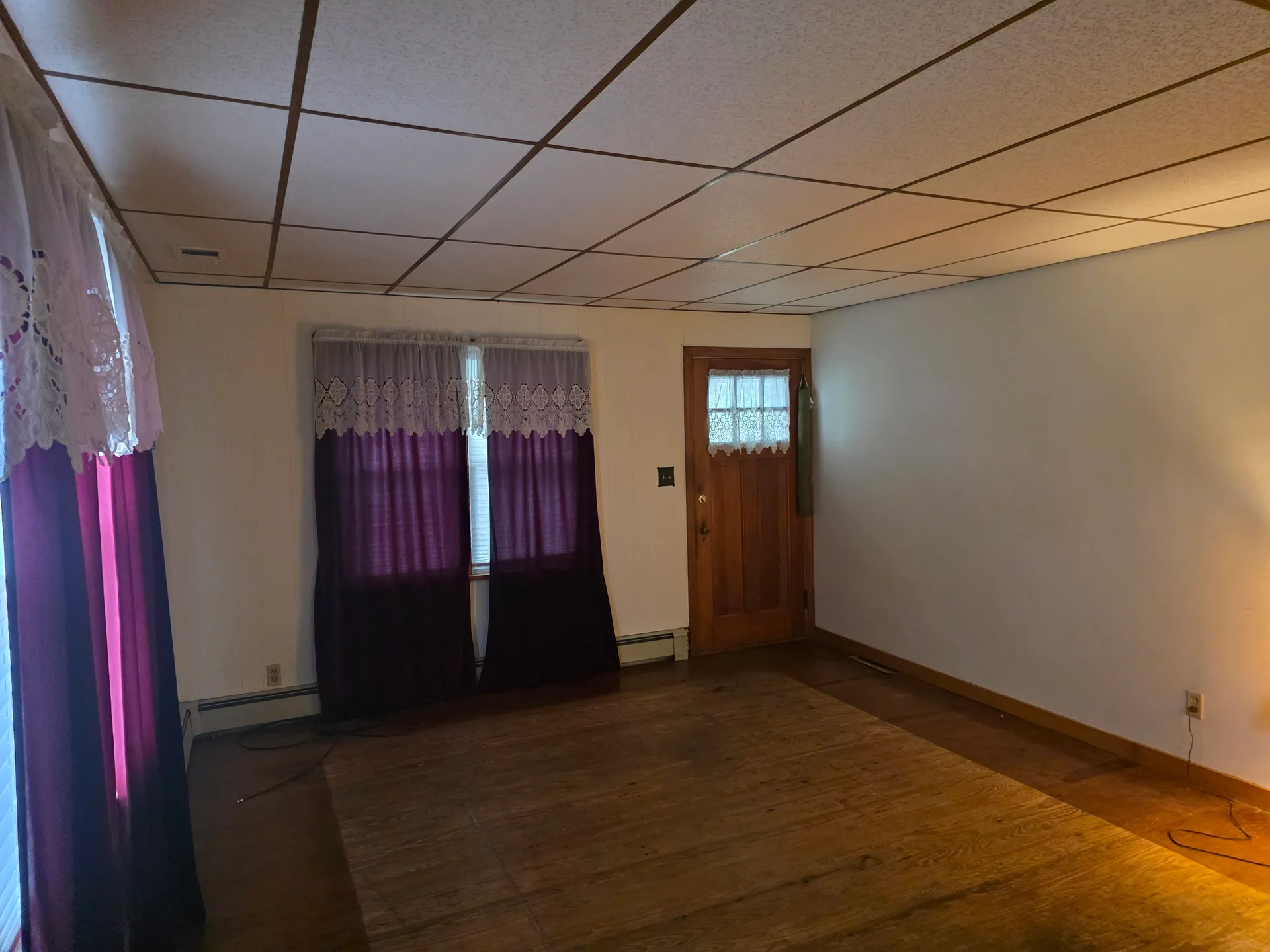 Living room with white walls, hardwood flooring, and drop ceiling tiles