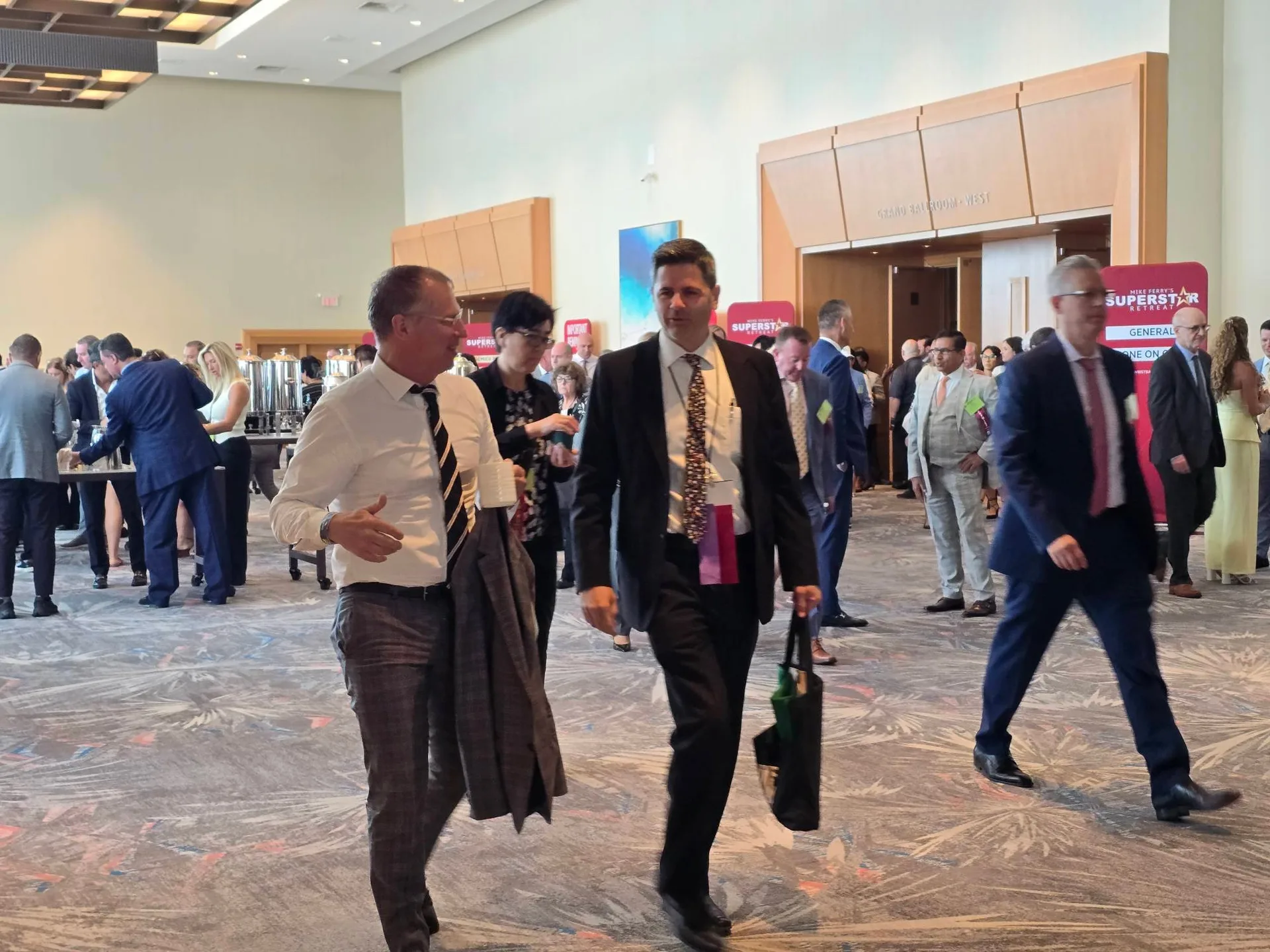 Attendees in business attire mingling and walking between sessions in the hallway at the Mike Ferry 2026 Superstar Retreat at The Diplomat Beach Resort in Hollywood, Florida, with SUPERSTAR event banners visible in the background