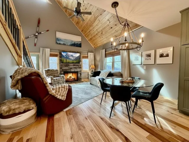 The open-concept living and dining room at Heart of Beech Retreat, with a stone fireplace and a wagon-wheel chandelier