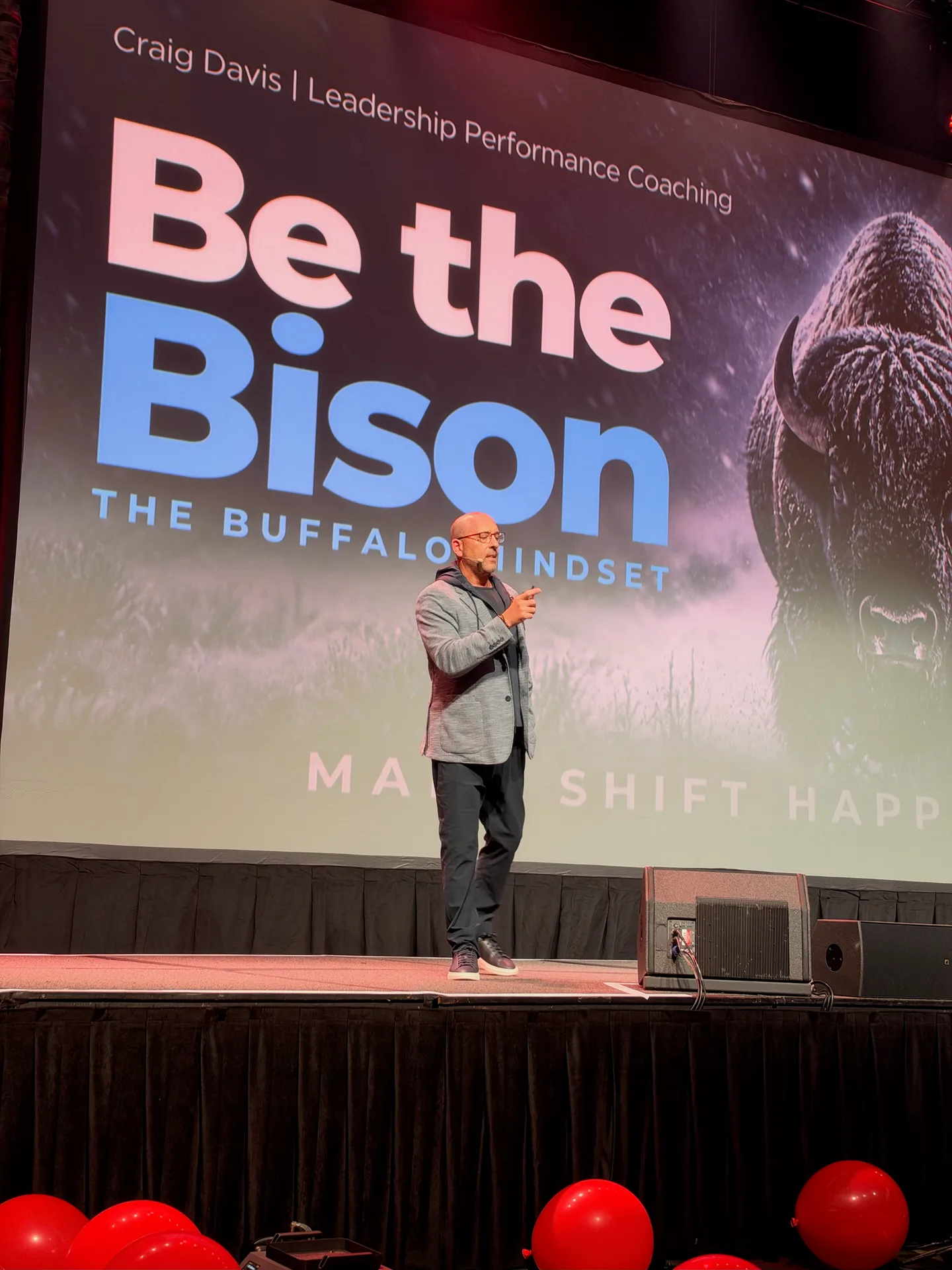Craig Davis center stage in a grey blazer in front of the Be the Bison: The Buffalo Mindset slide during his keynote at Momentum Builder Live