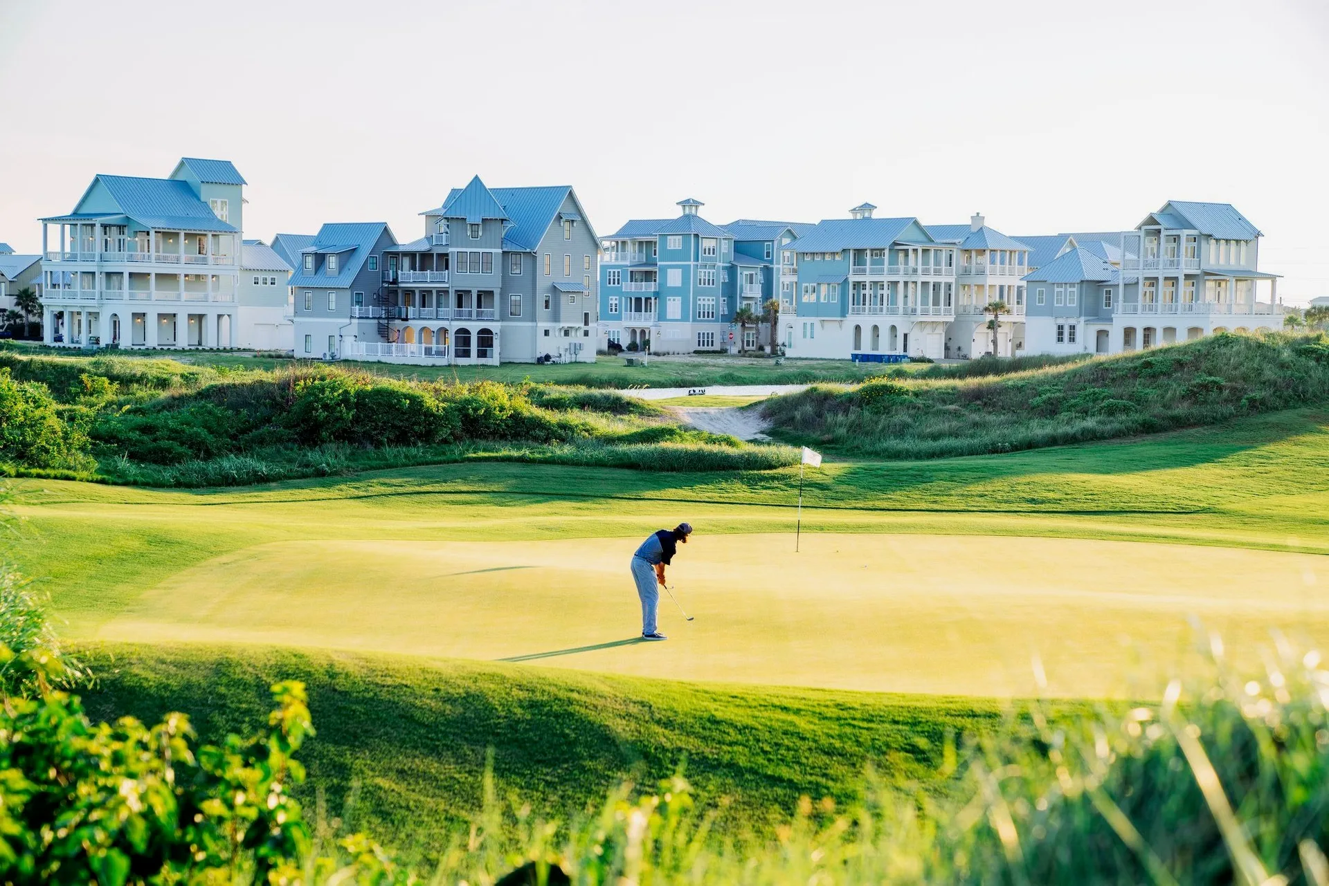 A golfer putting on a sunlit green with palms in the distance