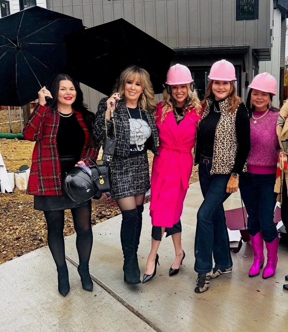 The Lioness Home Group team of five women, some in pink hard hats and rain gear with umbrellas, at the Ranch at Latitude 31 construction site in the rain