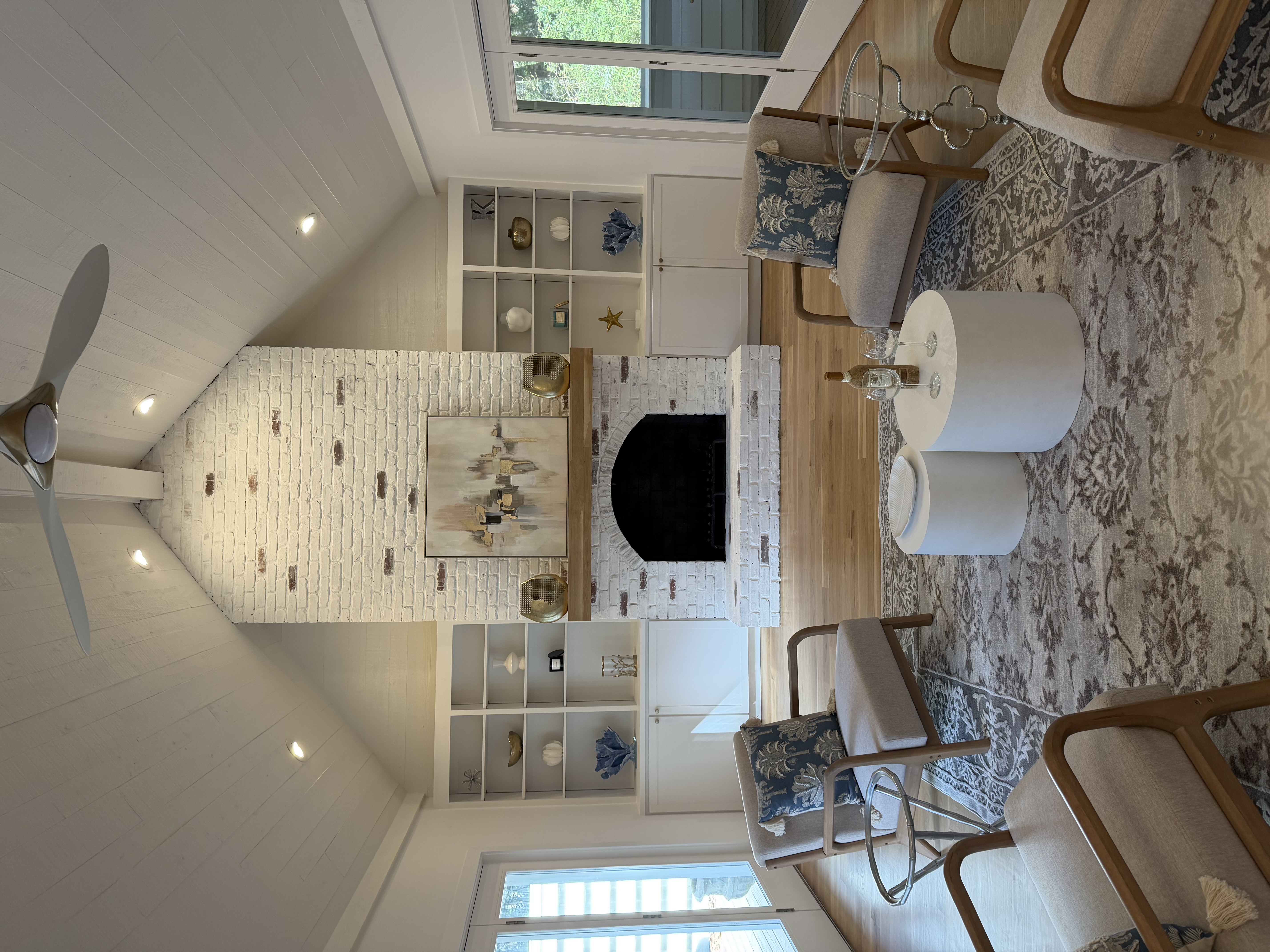 Bright coastal living room with a whitewashed brick fireplace, vaulted beamed ceiling, and French doors