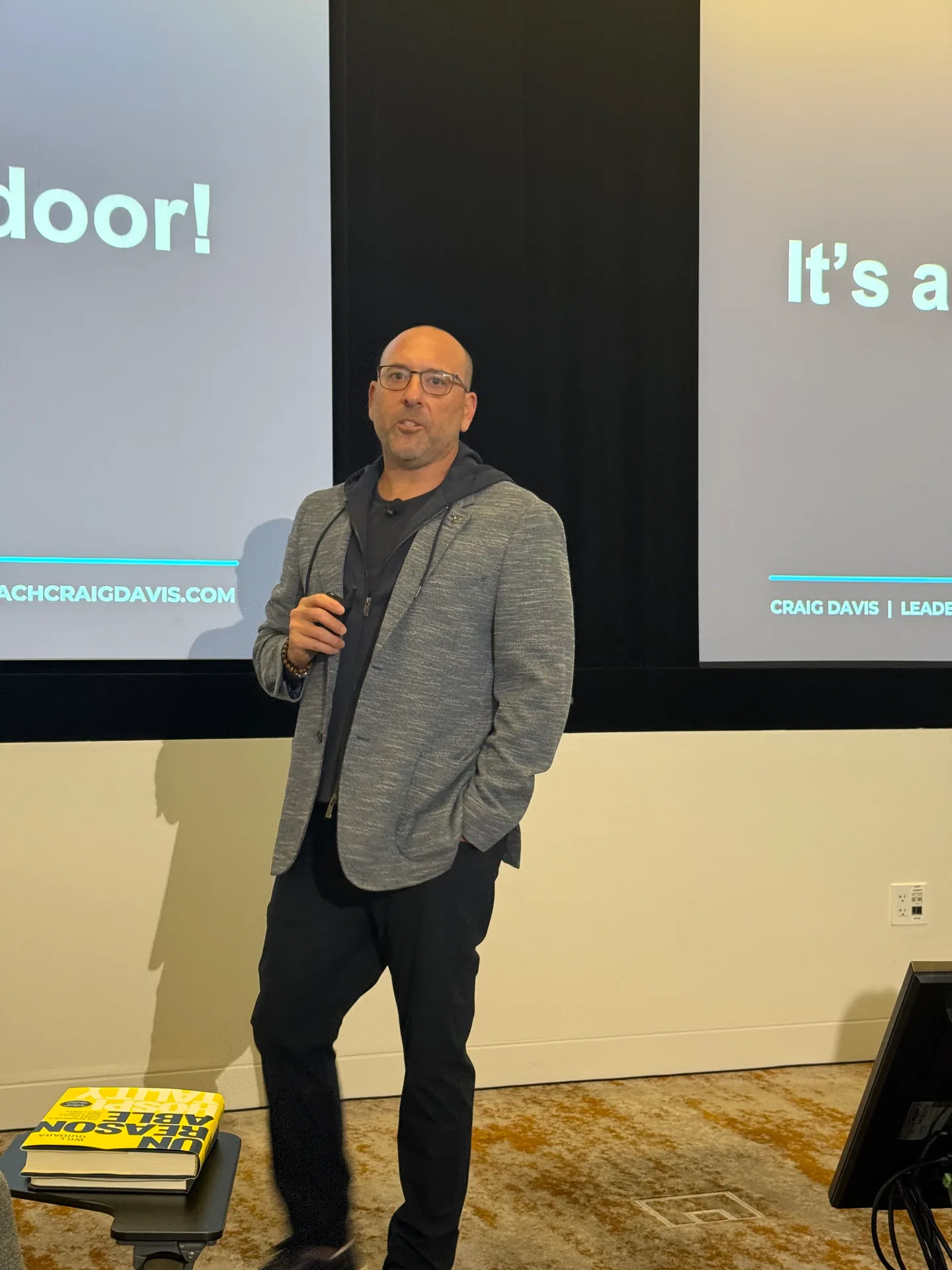 Craig Davis center stage in a grey blazer leading the workshop at the NFTYDoor Sales Summit, with two projector screens behind him
