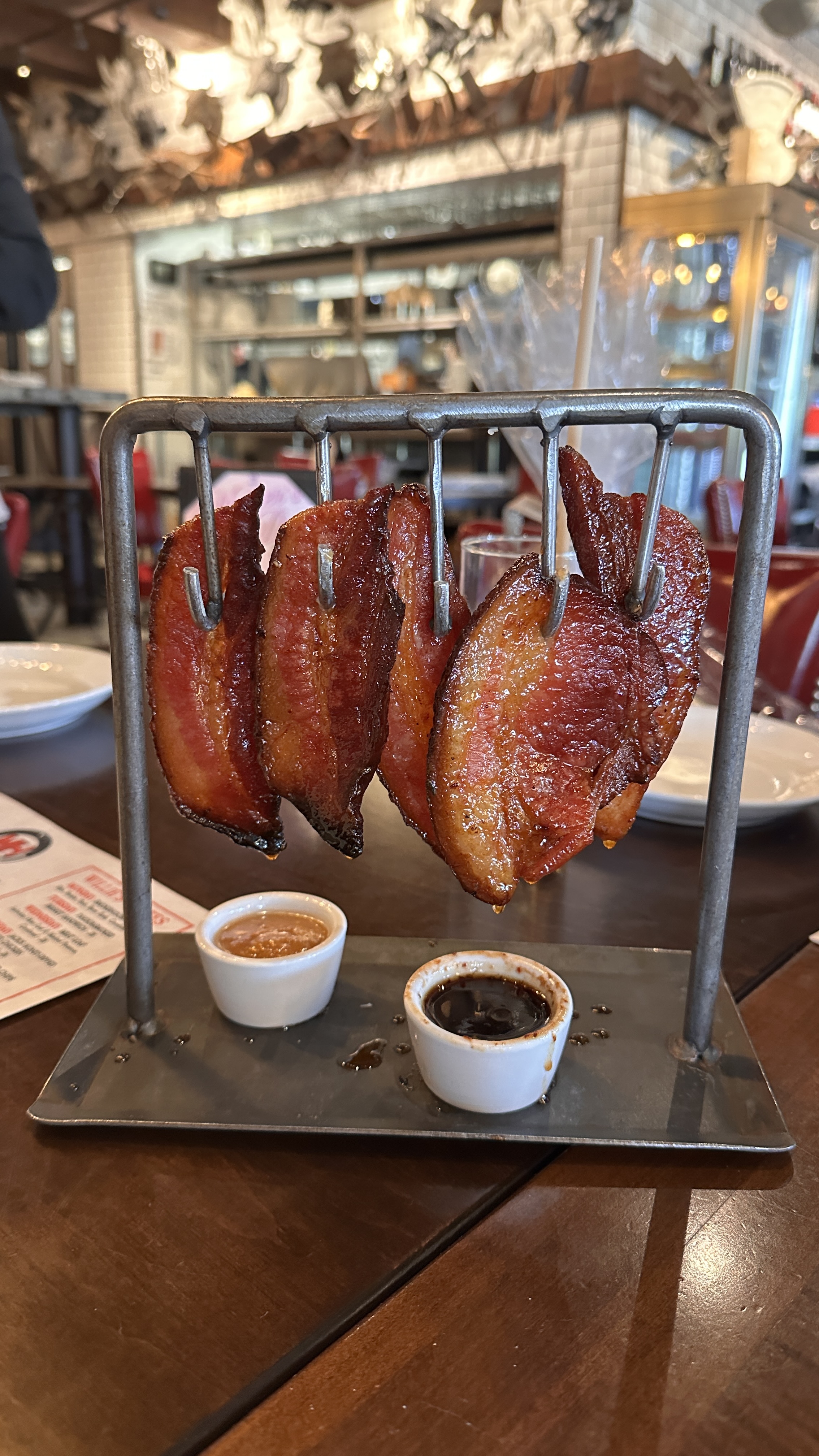Thick-cut bacon strips on a metal rack with dipping sauces, a must-try appetizer at Uncle Jack's Meat Market in Duluth Georgia