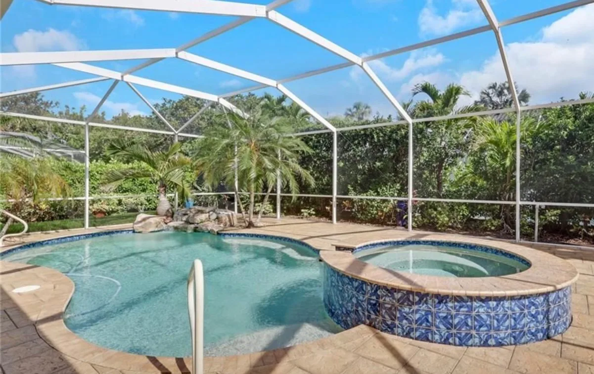 Screened-in pool and spa at 8711 Kilkenny Ct, with freeform pool, raised spa with blue tile, paved deck, and lush landscaping