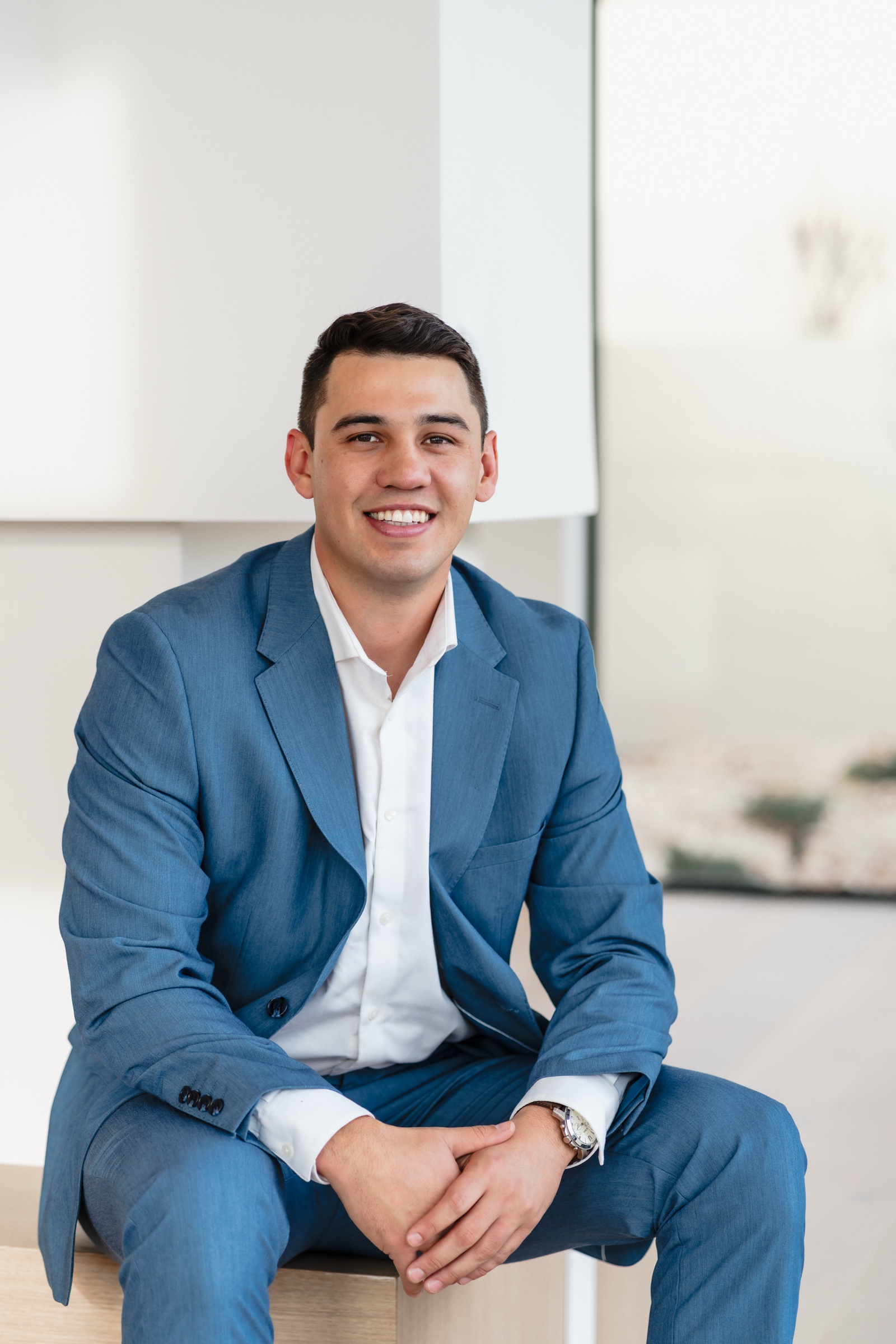 Professional 2026 portrait of Justin Murillo in a blue suit, seated and smiling
