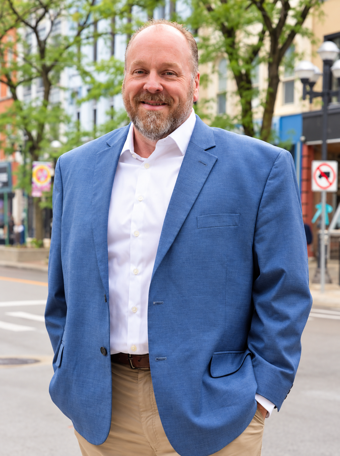 Bruce Heissenbuettel, a smiling man with a beard in a blue blazer, standing on an urban street