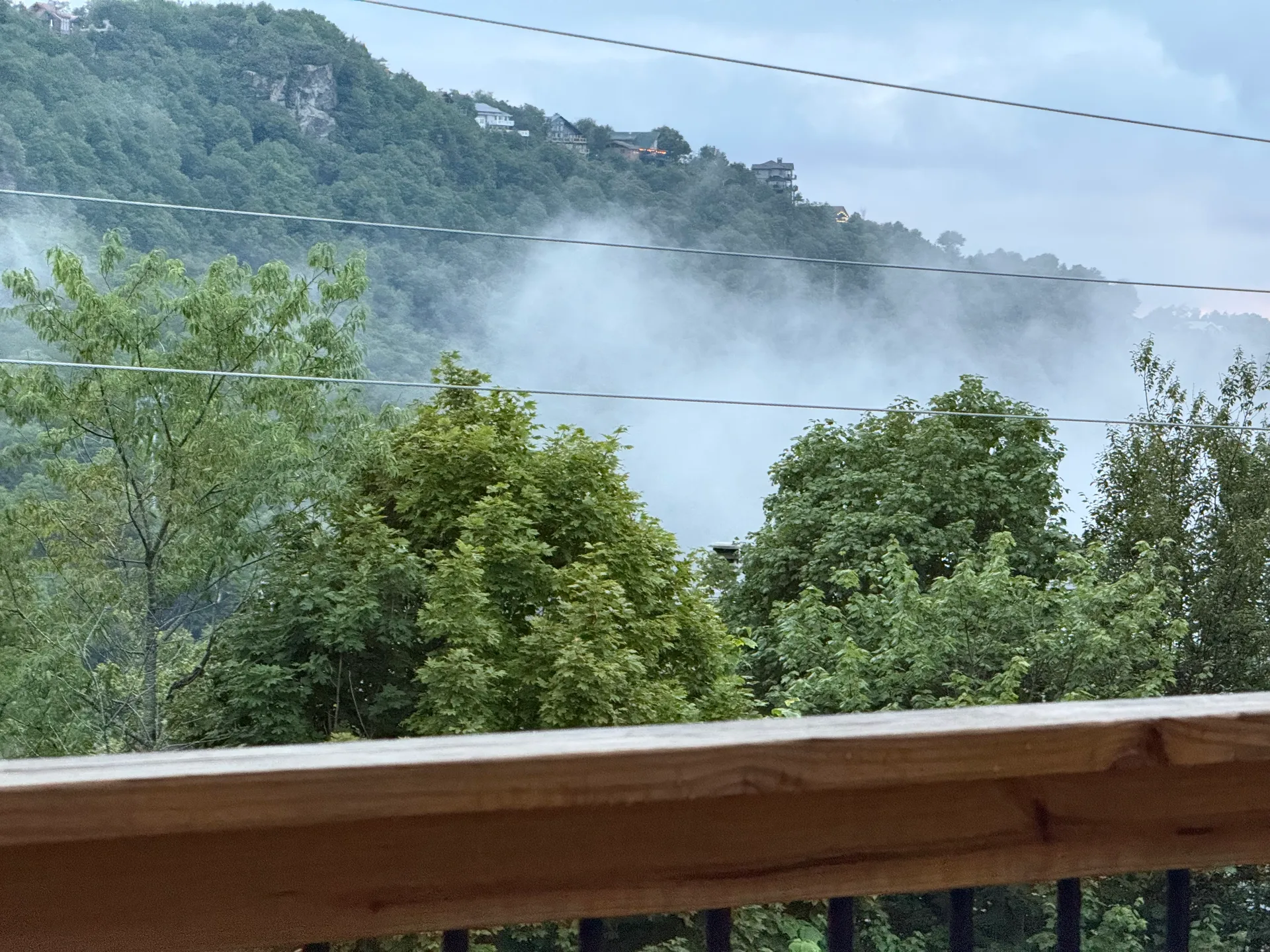 View from the cabin's back deck railing out over forested hills shrouded in mist and low clouds