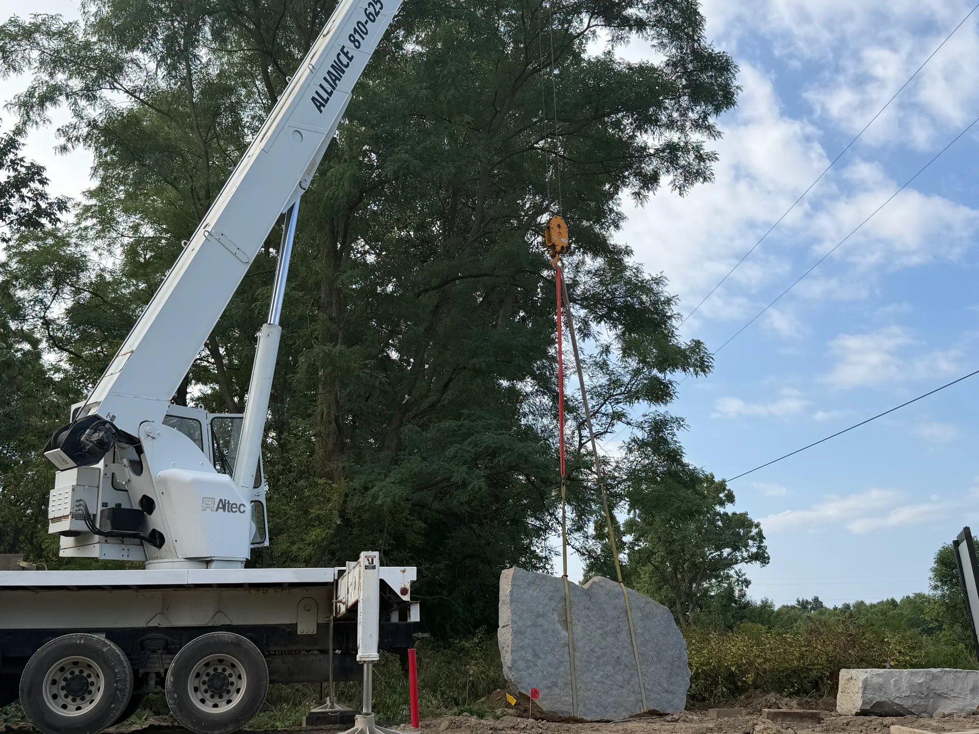 A massive 14,000-pound stone being lowered into place at the entrance of Oaks of Tyrone by heavy equipment in Tyrone Township Michigan