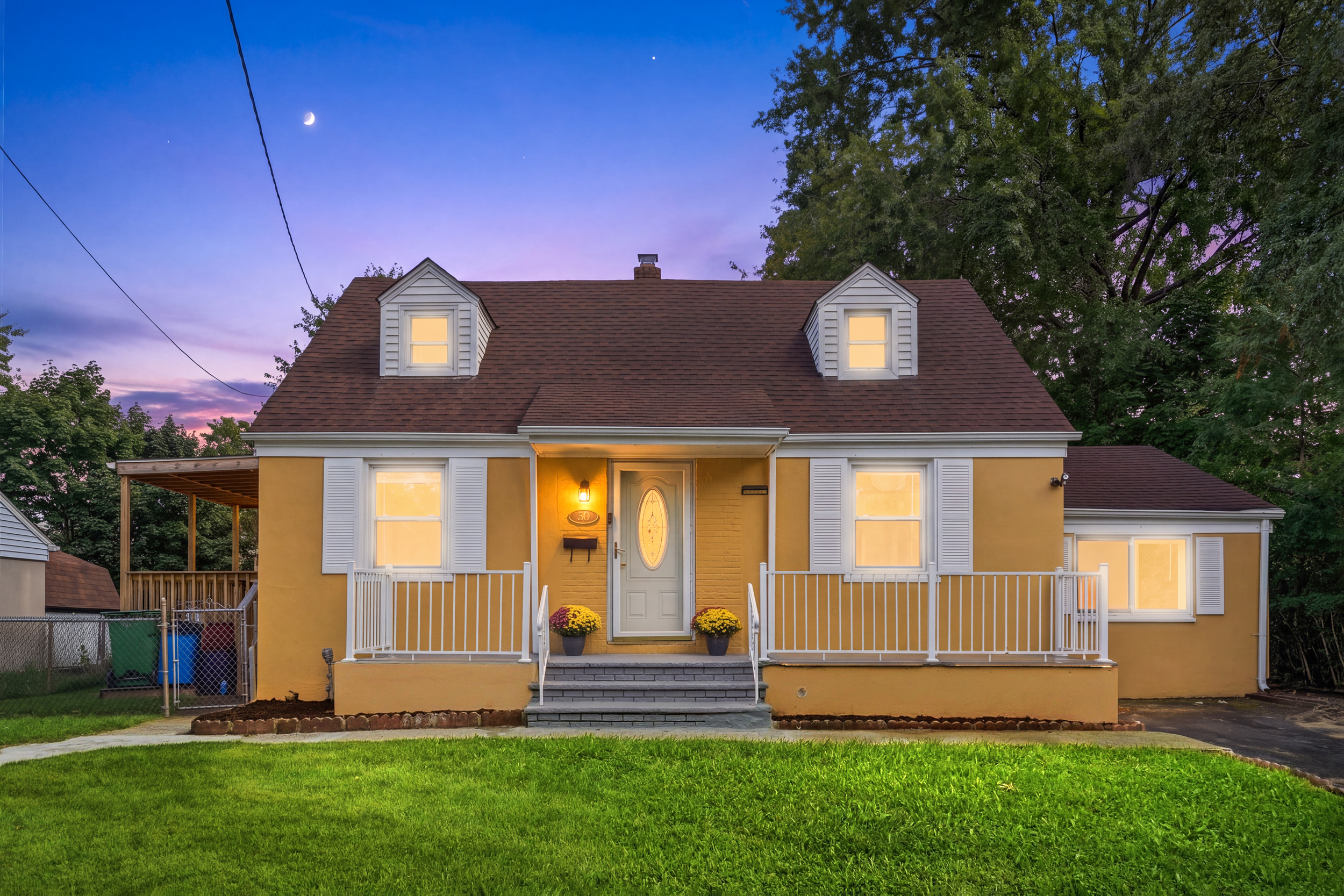 Twilight view of the front of the Cape Cod home at 50 Heather Ln with porch and interior lights glowing