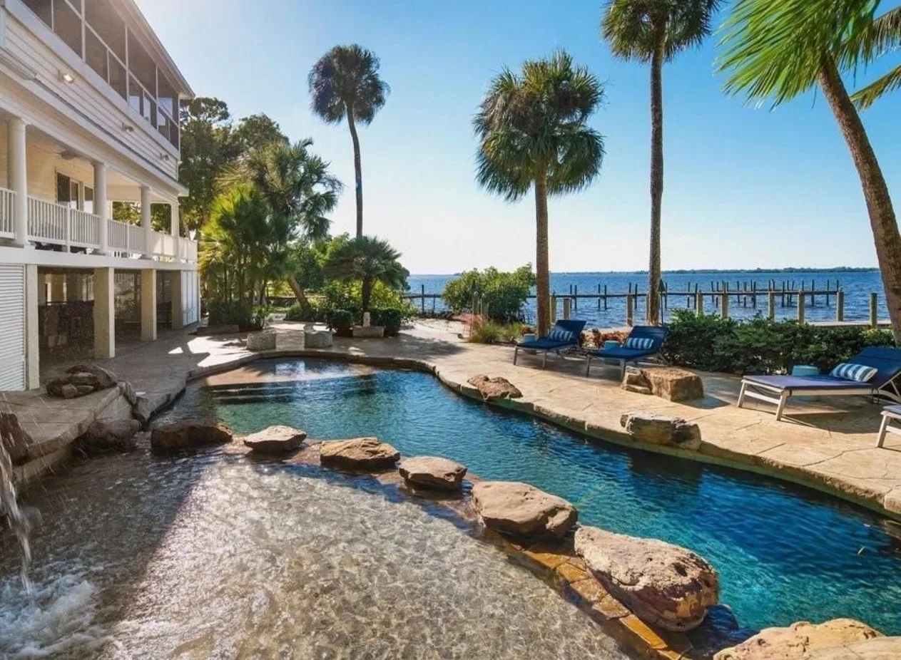 Pool with waterfall and stone deck surrounded by tropical landscaping with waterfront views at the historic estate