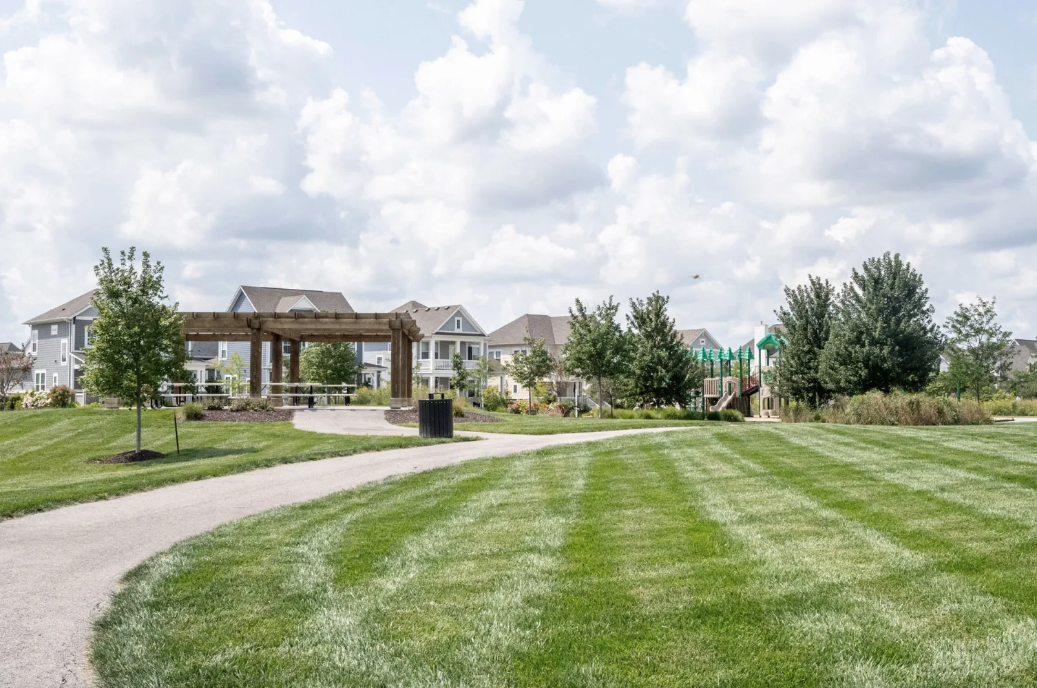 Neighborhood park with a wooden pergola, paved walking path, and shaded playground