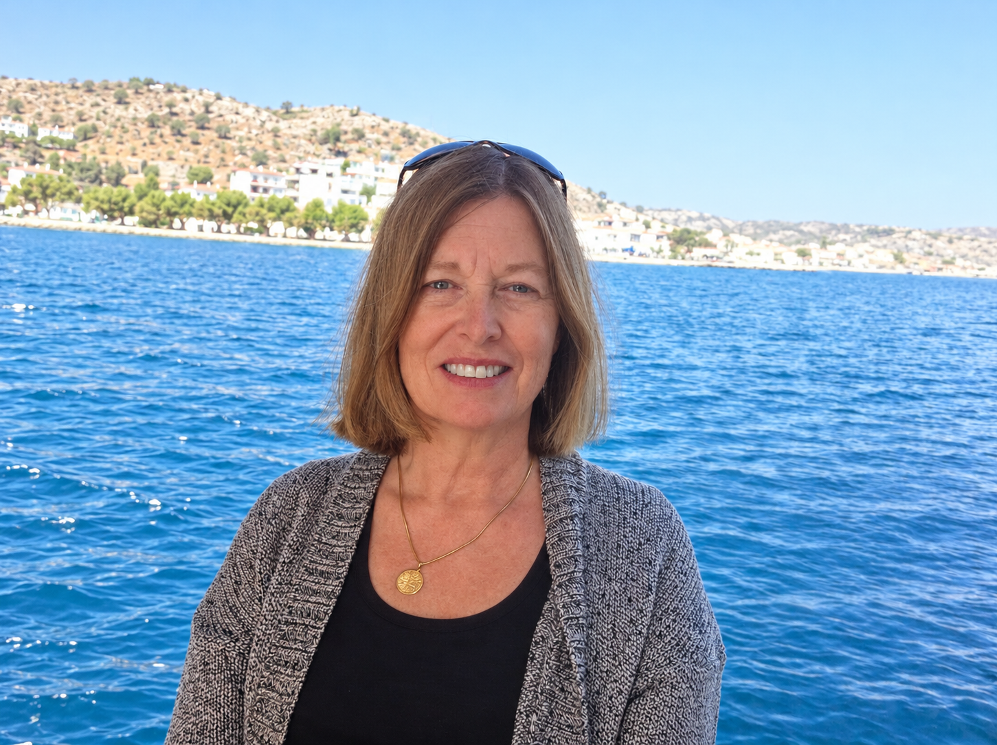 Carol aboard a boat, with blue sea and an island shoreline behind her.