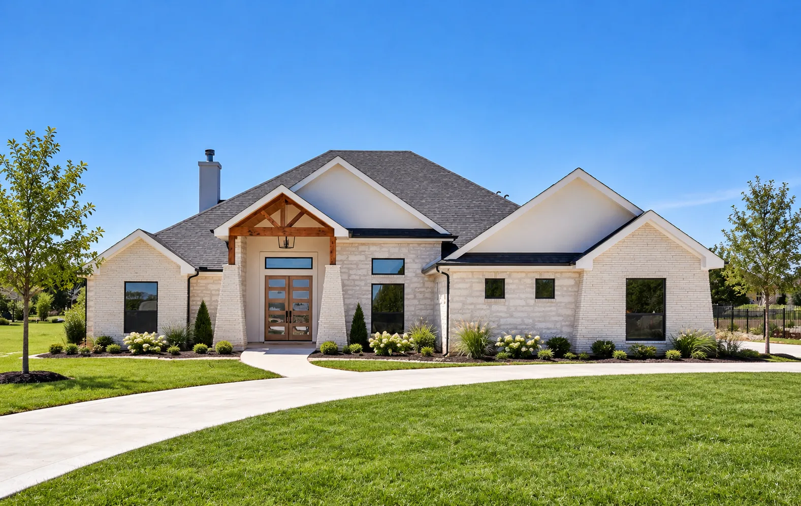 A Riata Builders custom home: a single-story modern farmhouse with an off-white stone veneer facade, white trim, and a timber-framed entry portico