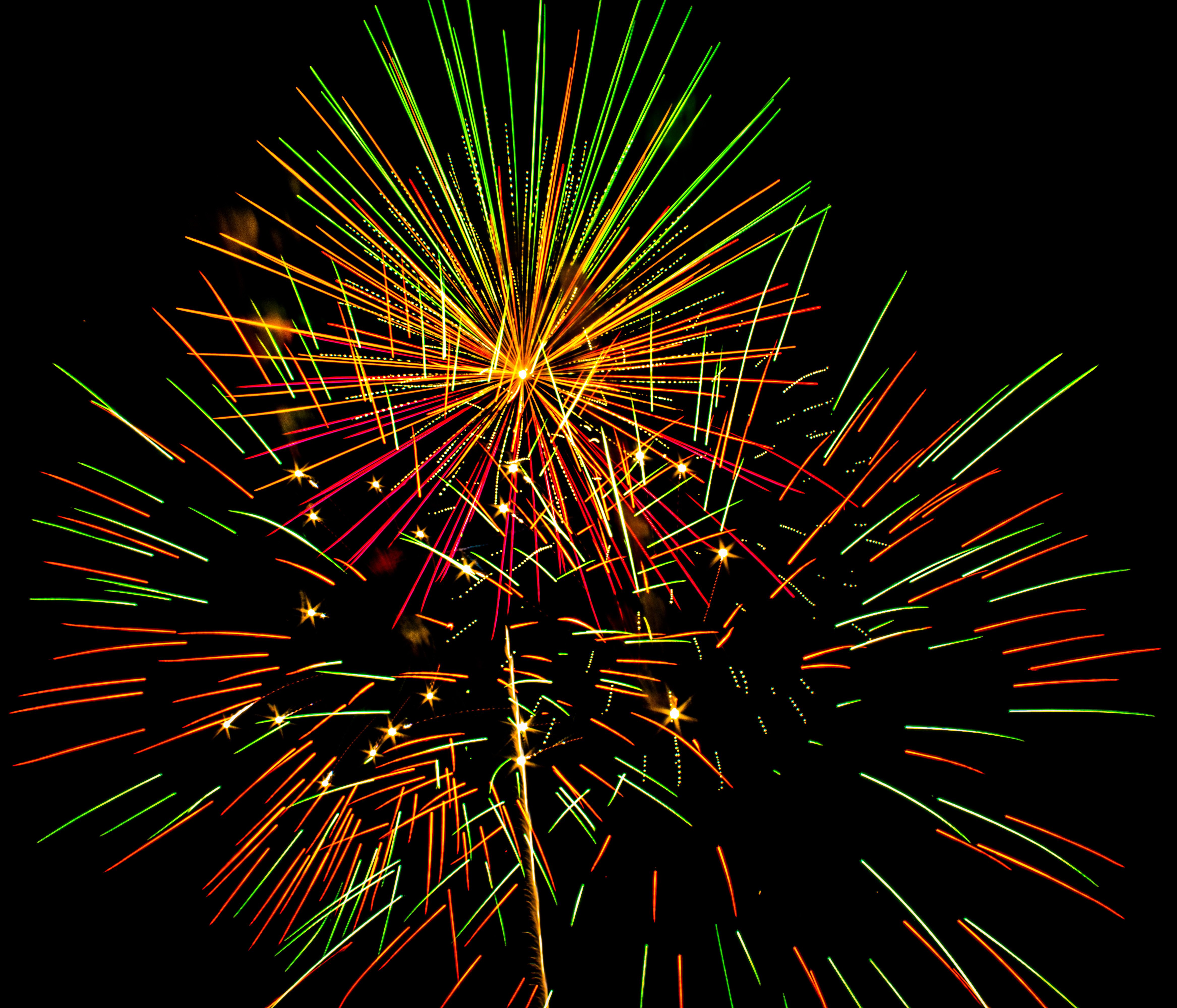 Festival scene with fireworks reflecting over water, vendor booths and community gathering visible in the foreground