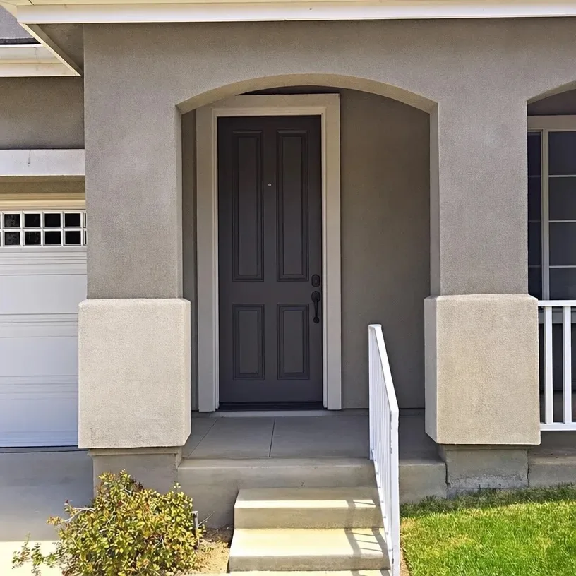 Gray stucco home exterior with covered porch entrance and mature landscaping