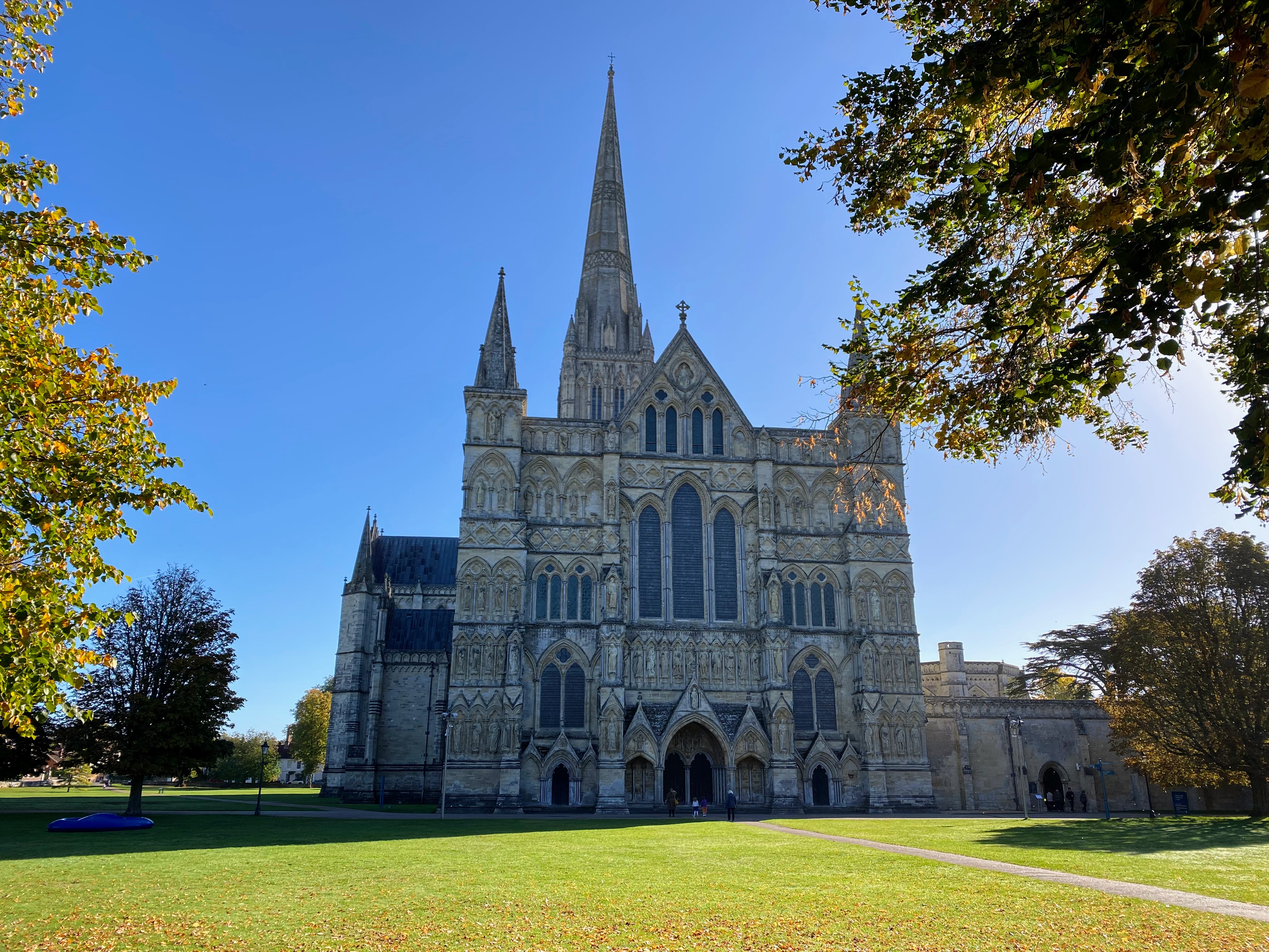 Salisbury Cathedral beneath a blue sky, framed by trees.
